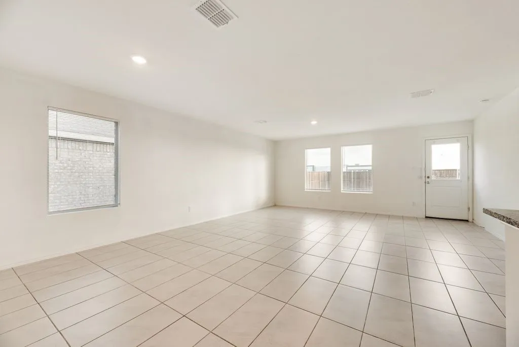 Expansive open-concept room featuring light-toned tile flooring, recessed ceiling lighting, multiple windows, and a rear exterior door