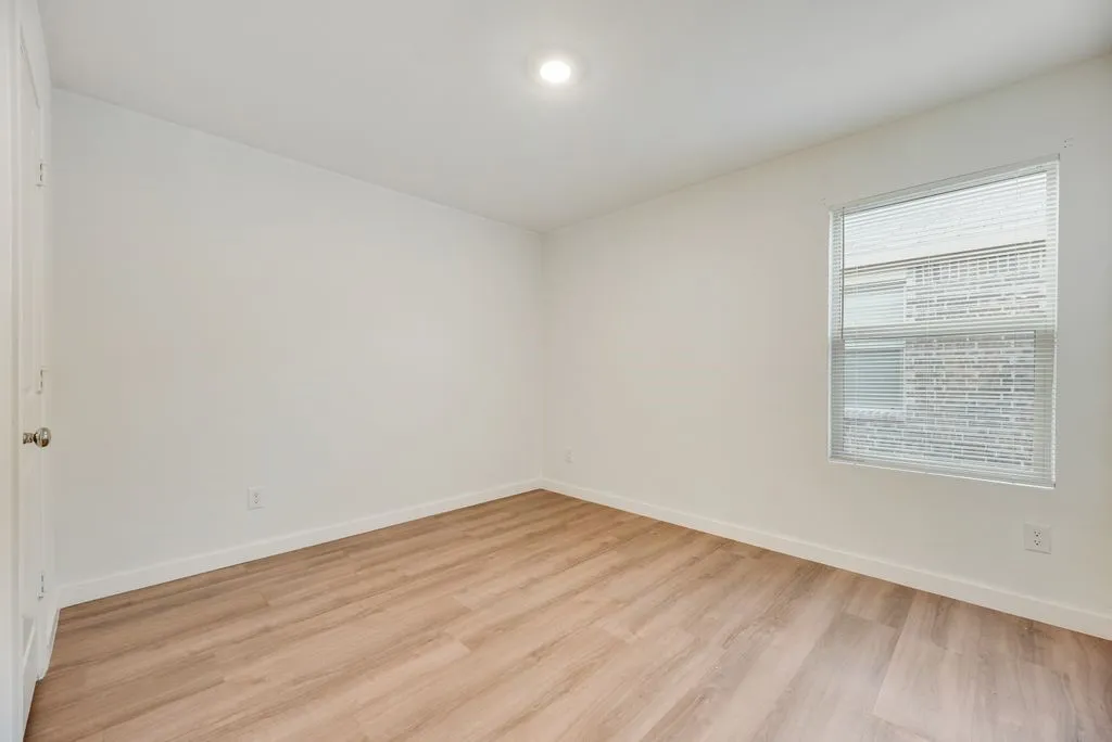 Room featuring wood-finish flooring, white baseboards, and a single window with blinds