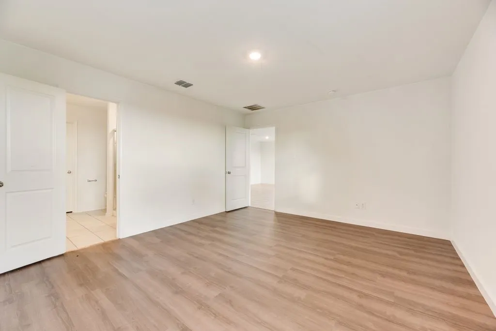 Spacious room with wood-finish flooring and neutral white walls