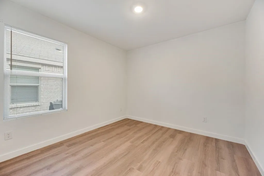 Bright interior space featuring a window with blinds, wood-finish flooring, white baseboards, a recessed ceiling light, and neutral wall tones