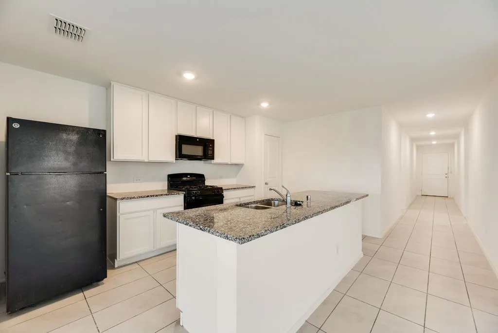 Kitchen featuring white cabinetry, black appliances, a stone-finish island with an integrated sink, and recessed lighting
