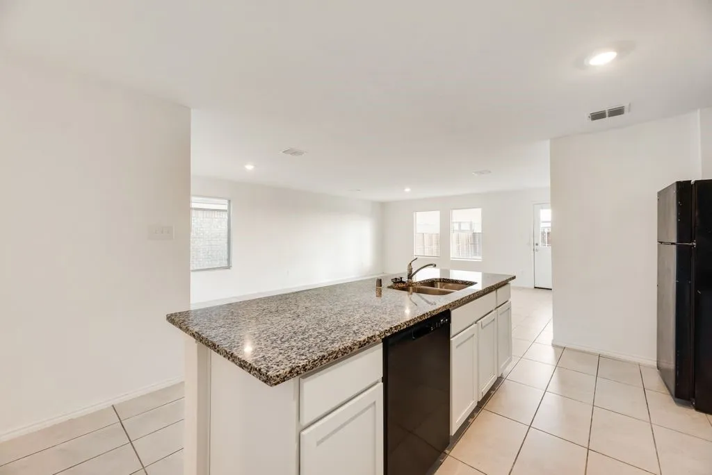 Kitchen island featuring a granite countertop, double basin sink, and integrated dishwasher