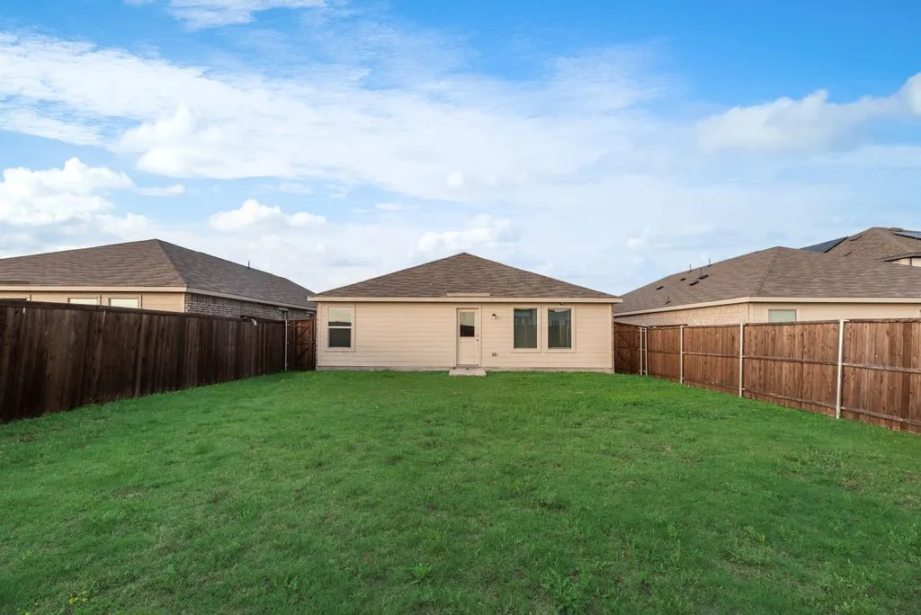 Expansive backyard with a manicured lawn, full wood fencing, and a light-colored exterior featuring multiple windows