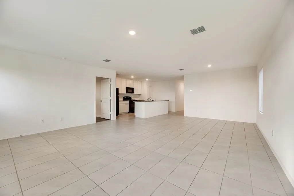Spacious open-concept interior featuring light-colored tile flooring, recessed lighting, and a kitchen with white cabinetry, dark countertops, and black appliances