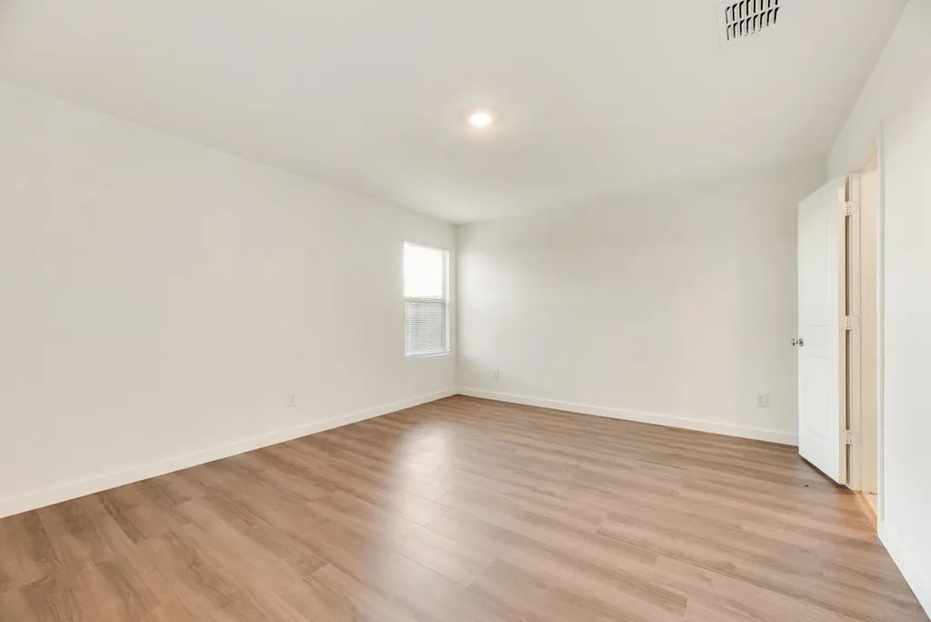 Spacious room featuring wood-finish flooring, white baseboards, and a single window with blinds