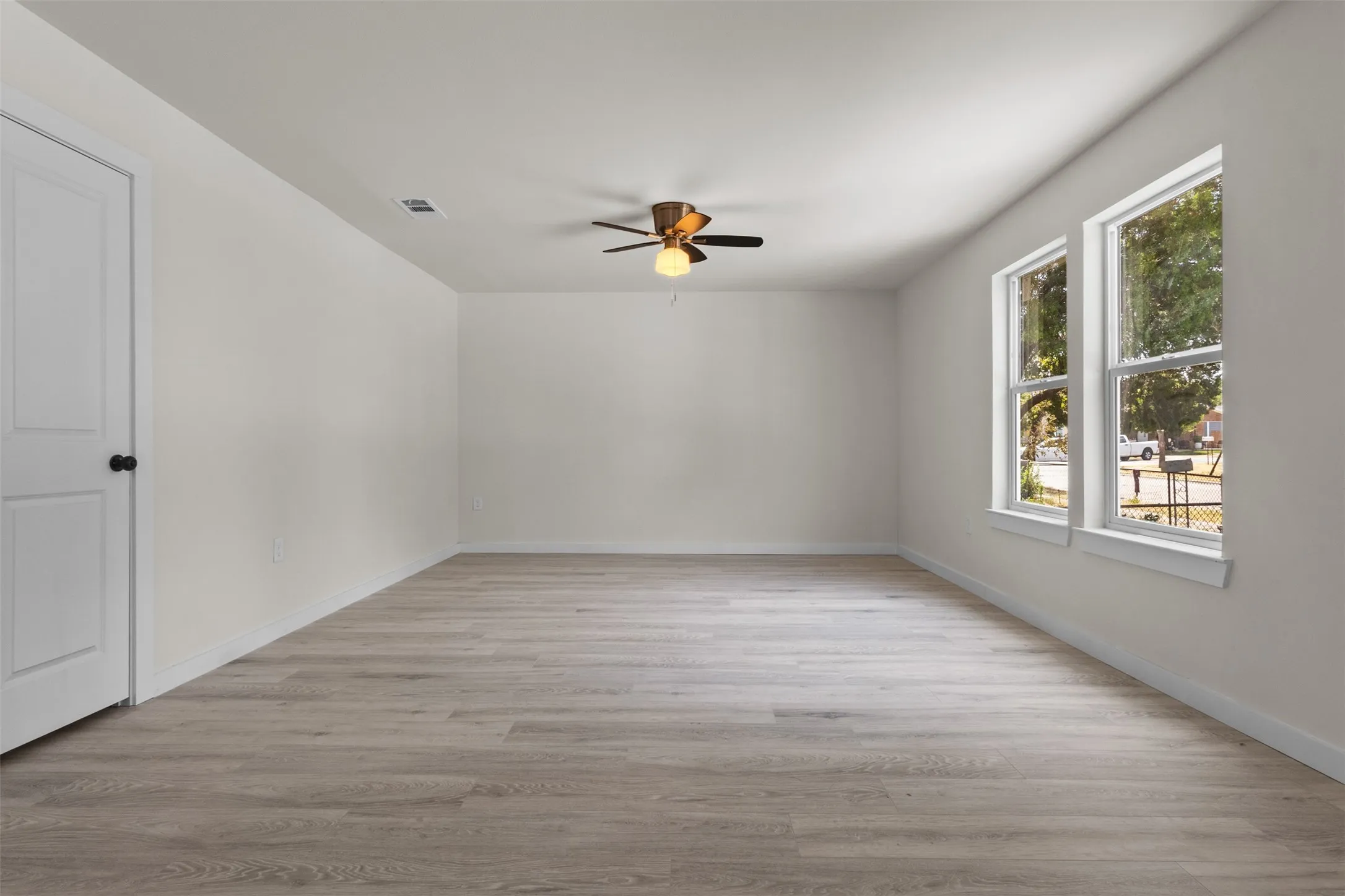 Spacious room featuring wood-finish flooring, white painted walls, a ceiling fan with integrated lighting, and two double-hung windows