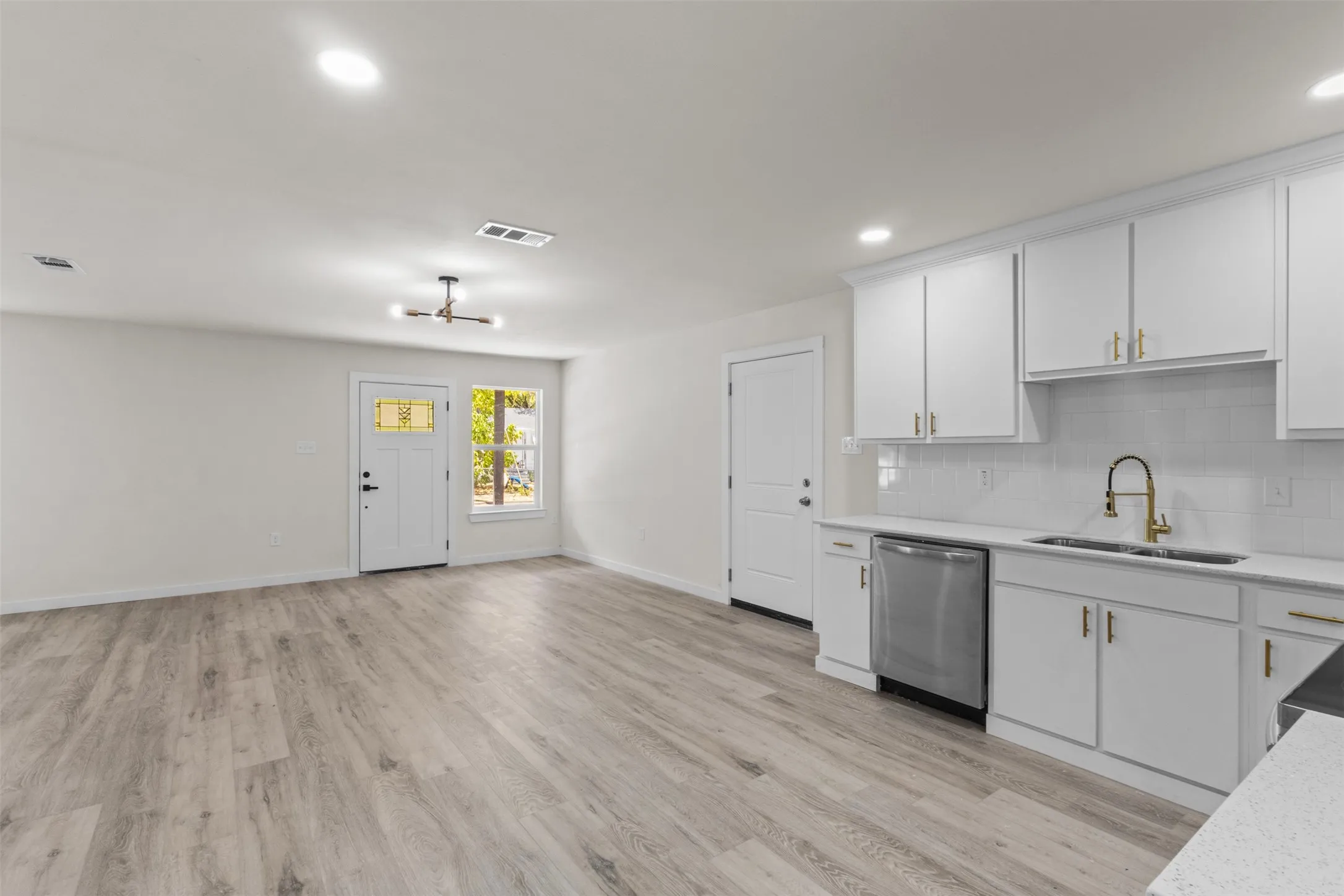 Wood-finish flooring throughout, recessed lighting, white kitchen cabinetry with gold-finish hardware, stainless steel dishwasher, and a white subway tile backsplash