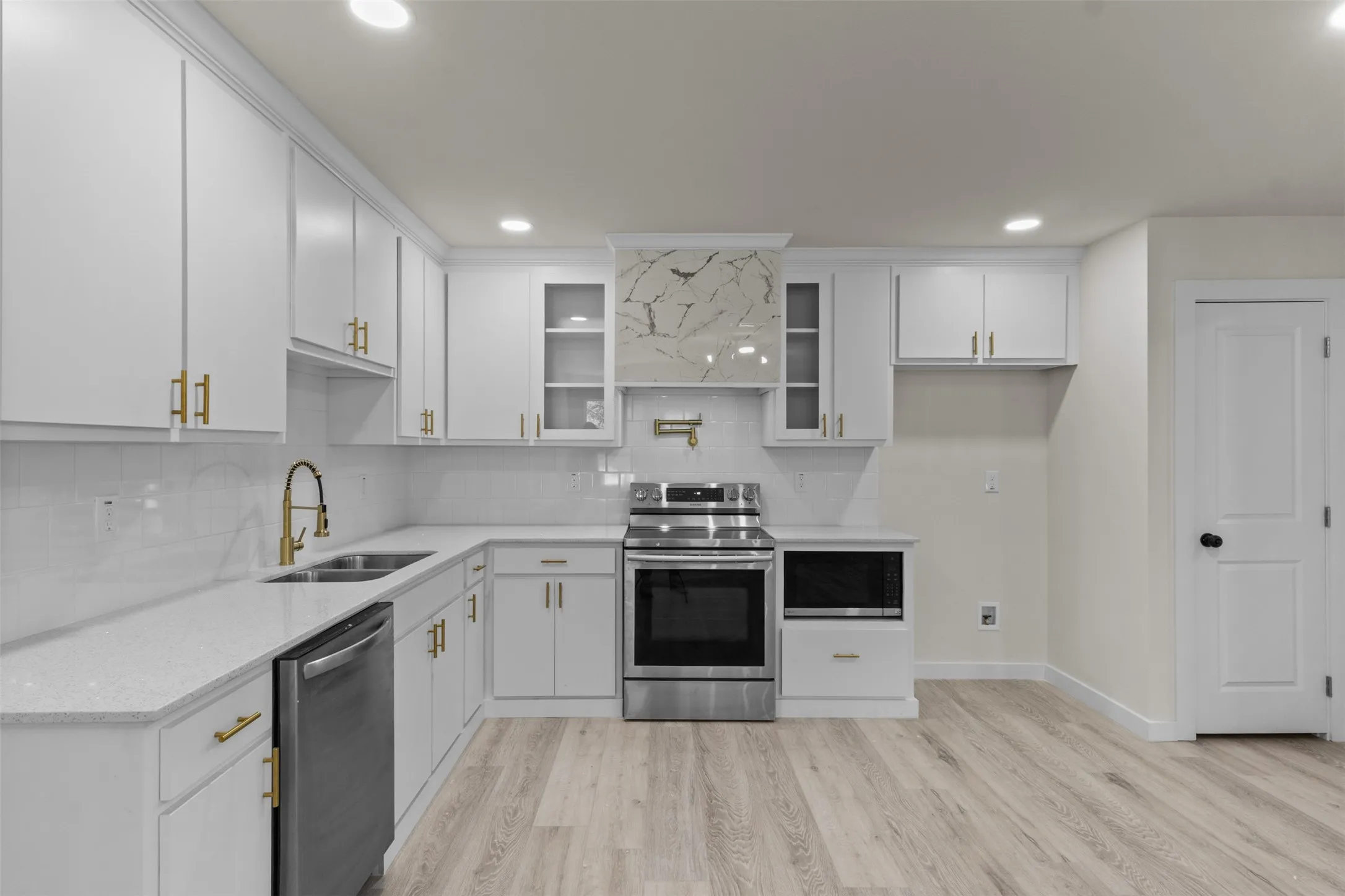 White cabinetry with gold-finish hardware, stainless steel appliances, a tile backsplash, and wood-finish flooring