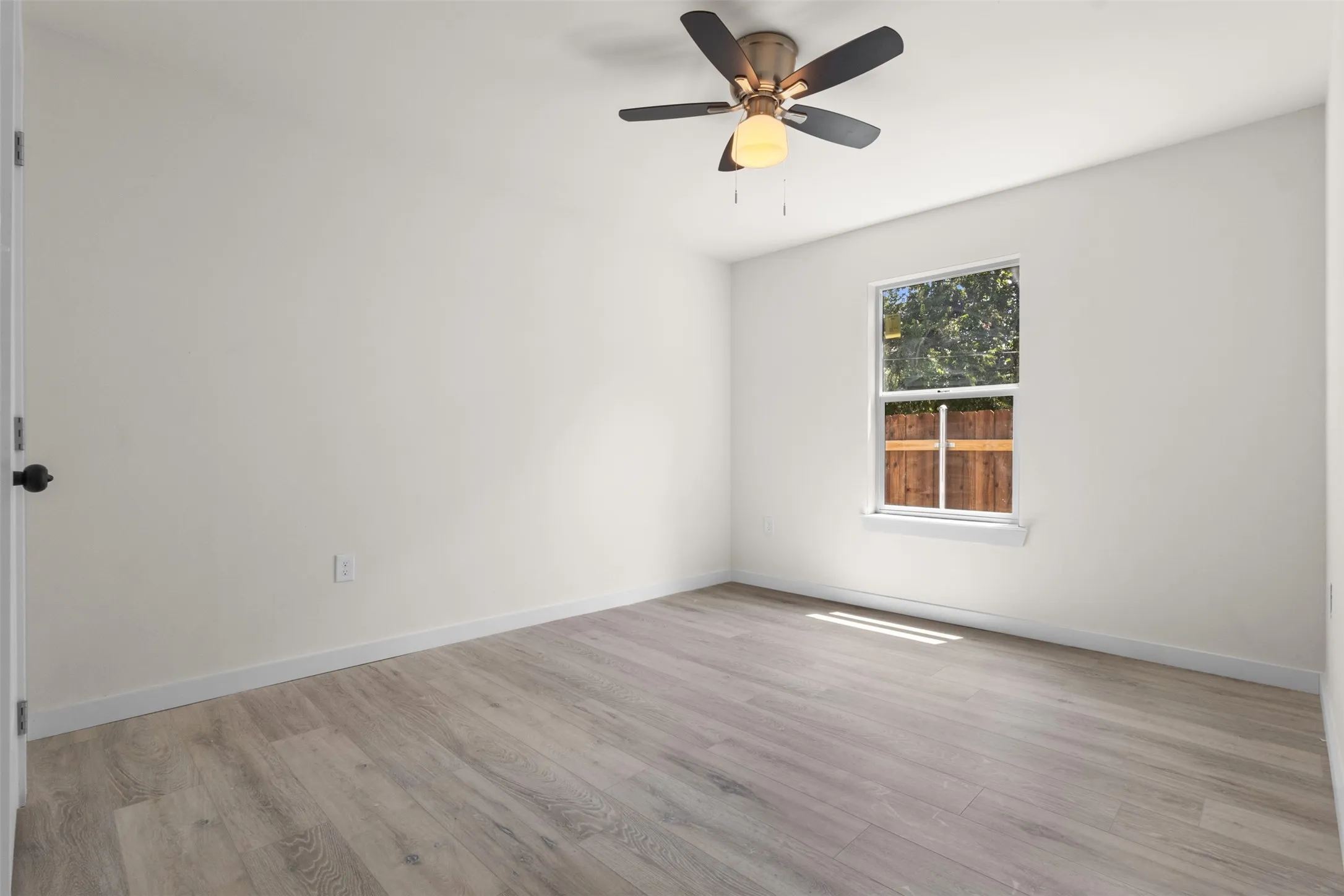 Spacious room featuring wood-finish flooring, a ceiling fan with integrated lighting, and a window providing natural illumination