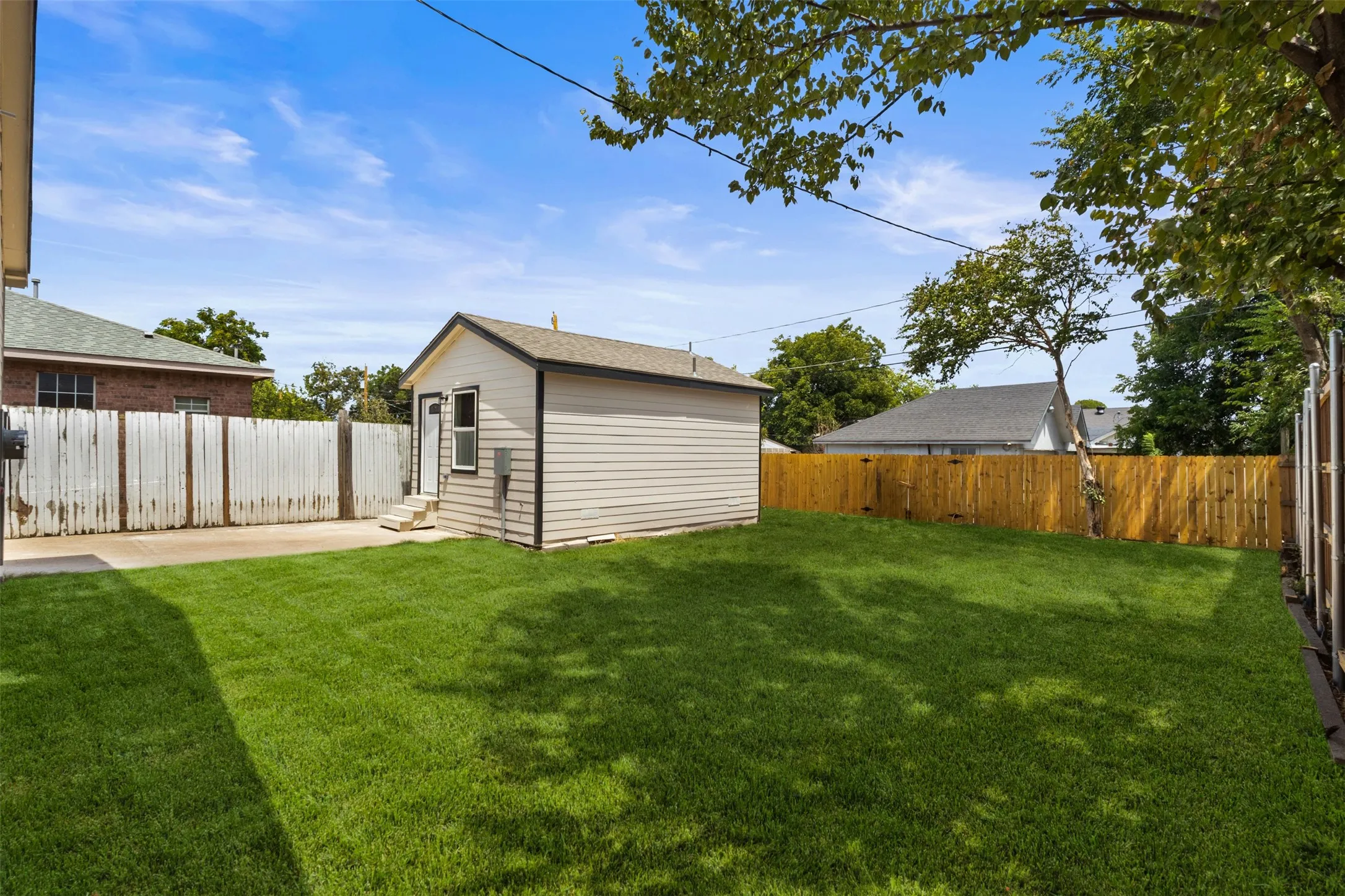 Expansive lawn area with a separate outbuilding, a concrete pad, and wood fencing