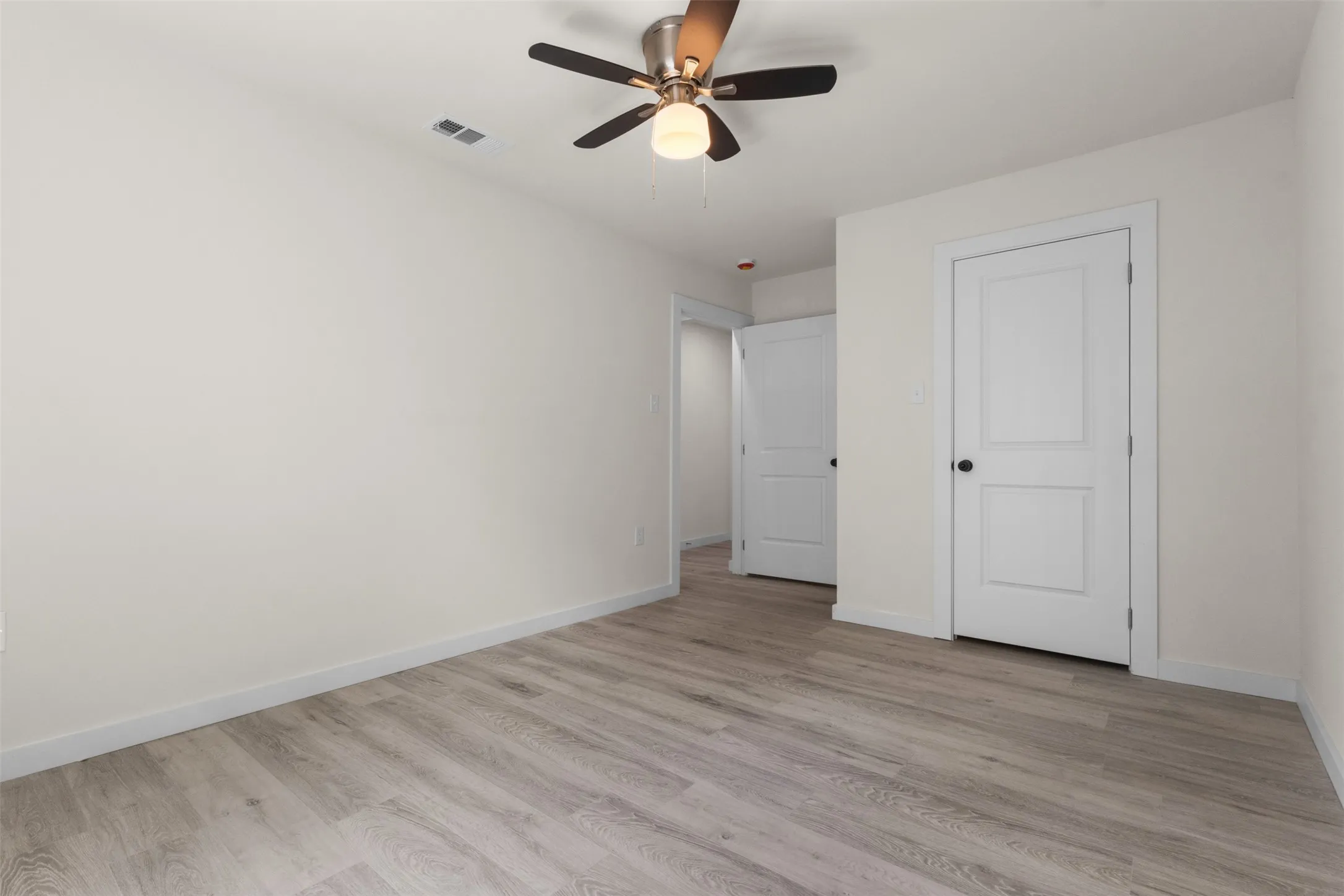 Wood-finish flooring, white walls, two-panel interior doors, and a ceiling fan with integrated lighting