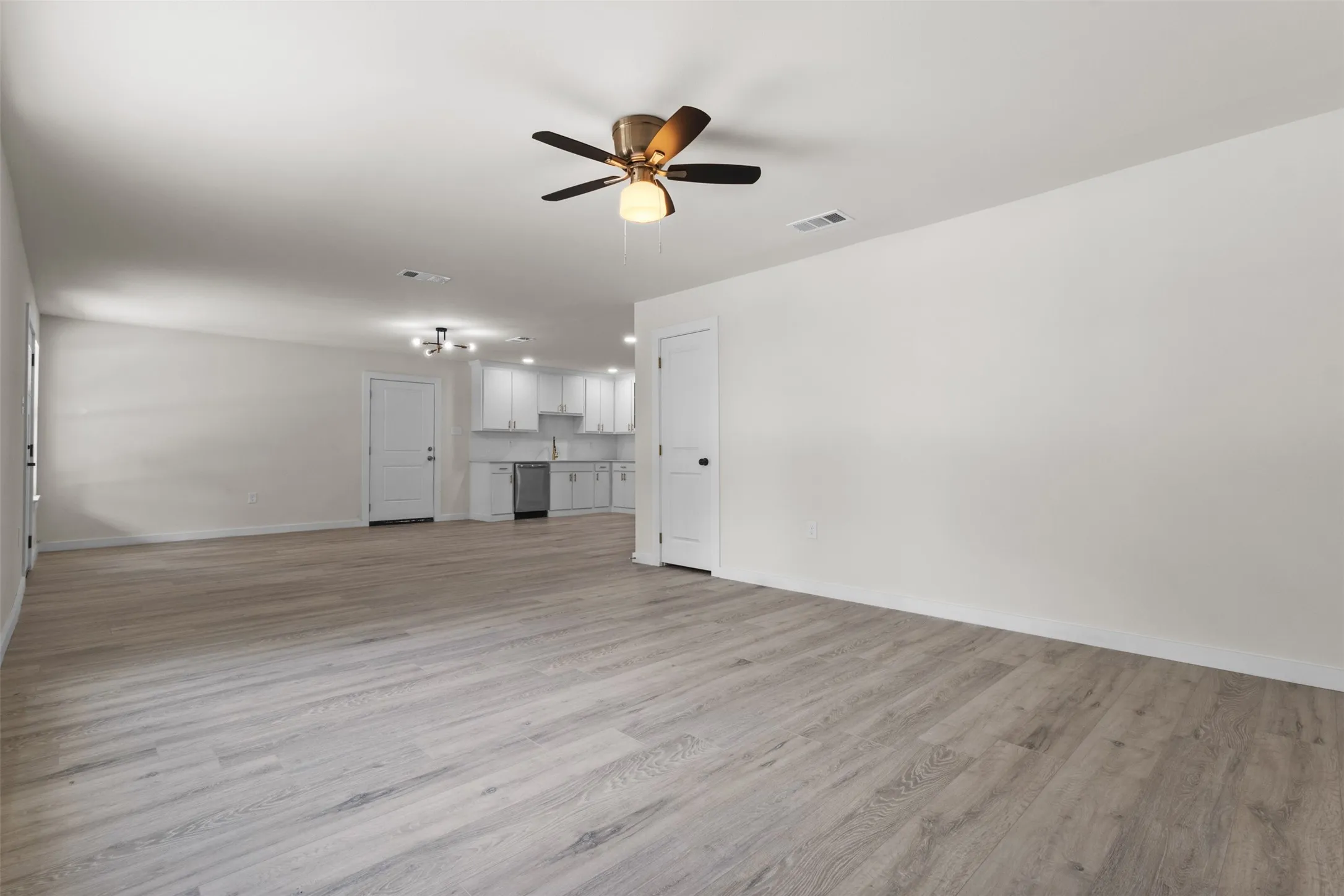 Spacious room featuring wood-finish flooring, a ceiling fan, and white walls