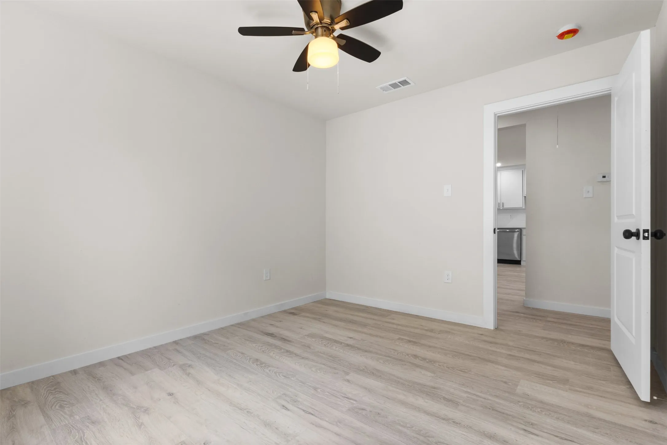 Light wood-finish flooring, ceiling fan with integrated lighting, and white walls