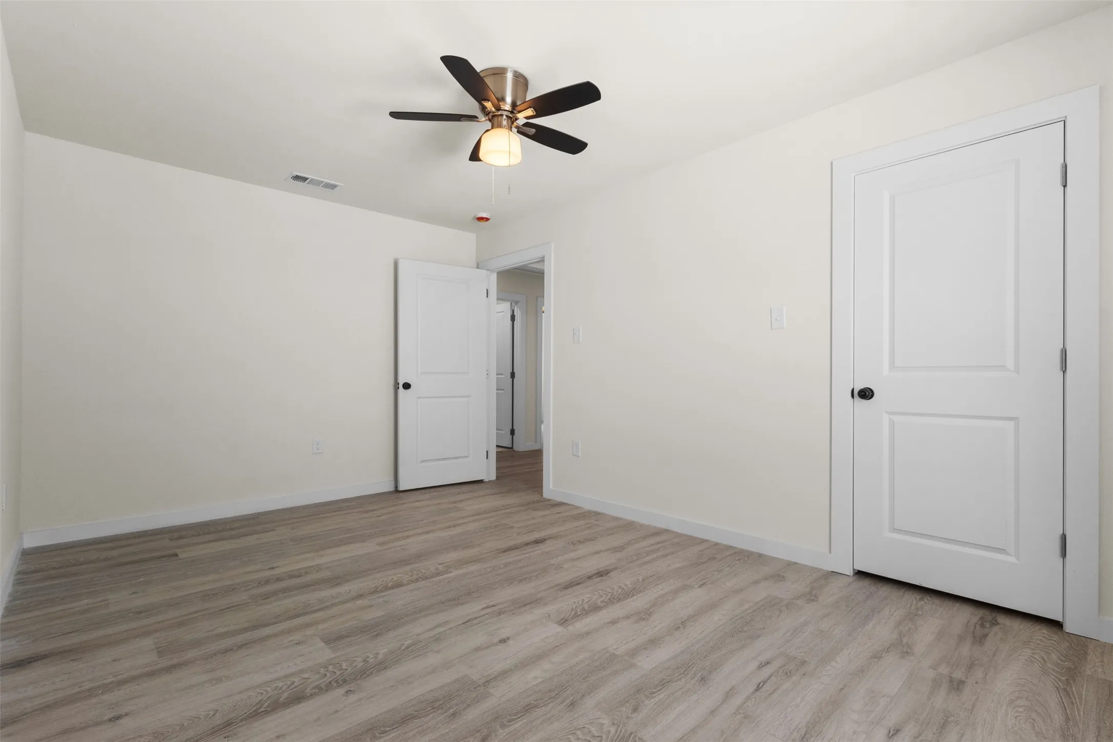 Neutral-toned wood-finish flooring, white walls, and a ceiling fan with integrated lighting