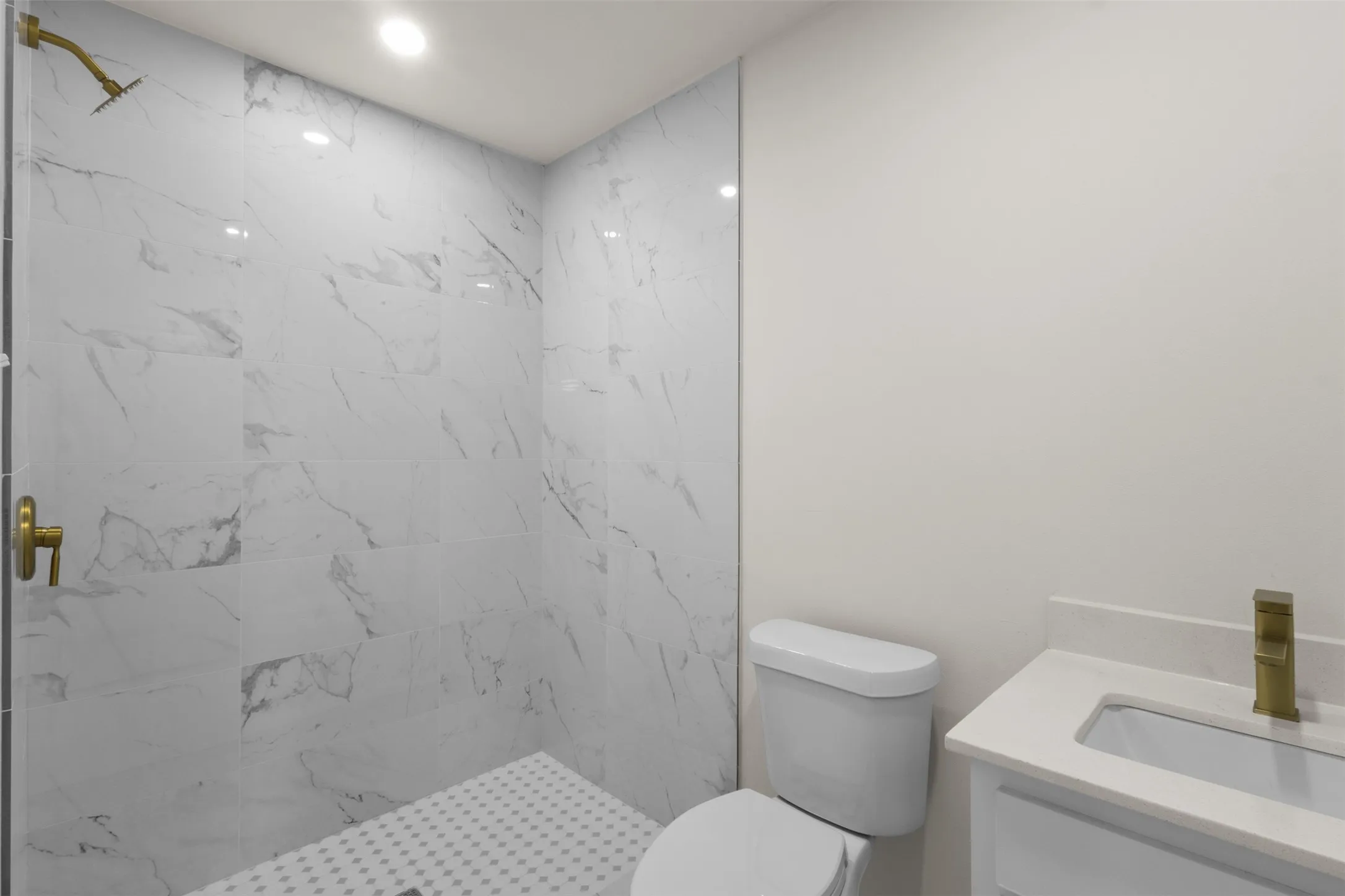 Walk-in shower with large format tile, brushed gold fixtures, recessed lighting, white vanity with integrated sink, and white countertop
