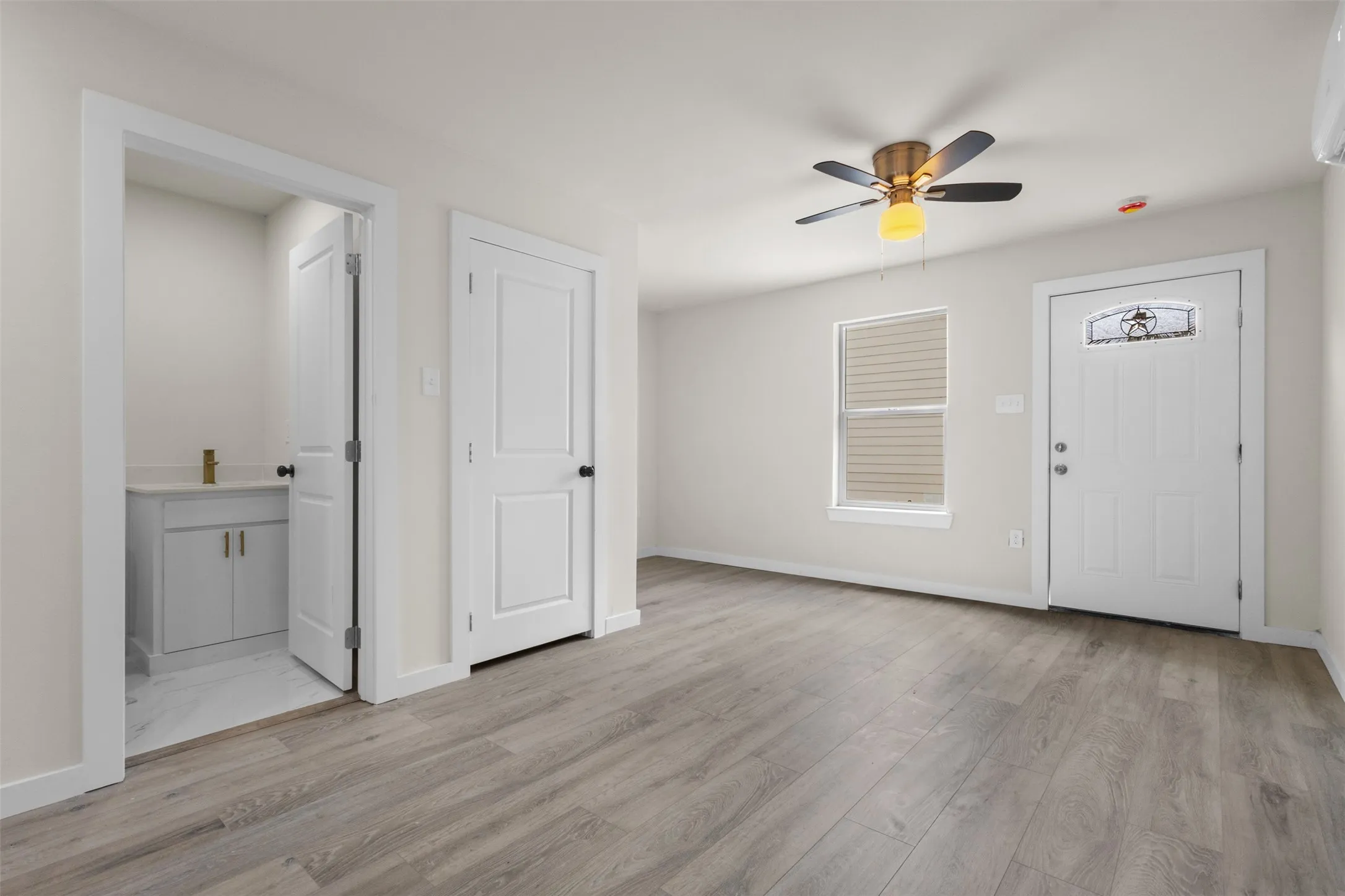 Wood-finish flooring, white paneled doors, ceiling fan with integrated lighting, and a front entry door with decorative glass
