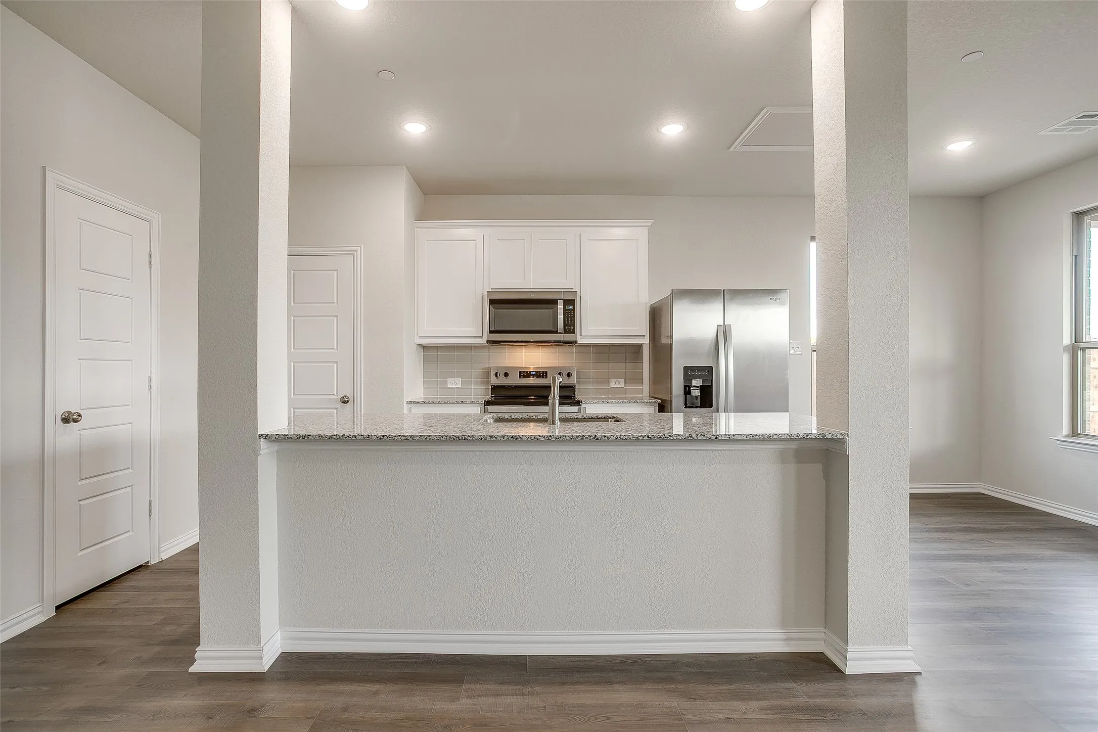 Kitchen featuring white cabinetry, light stone countertops, decorative backsplash, stainless steel appliances, and dark wood finished floors