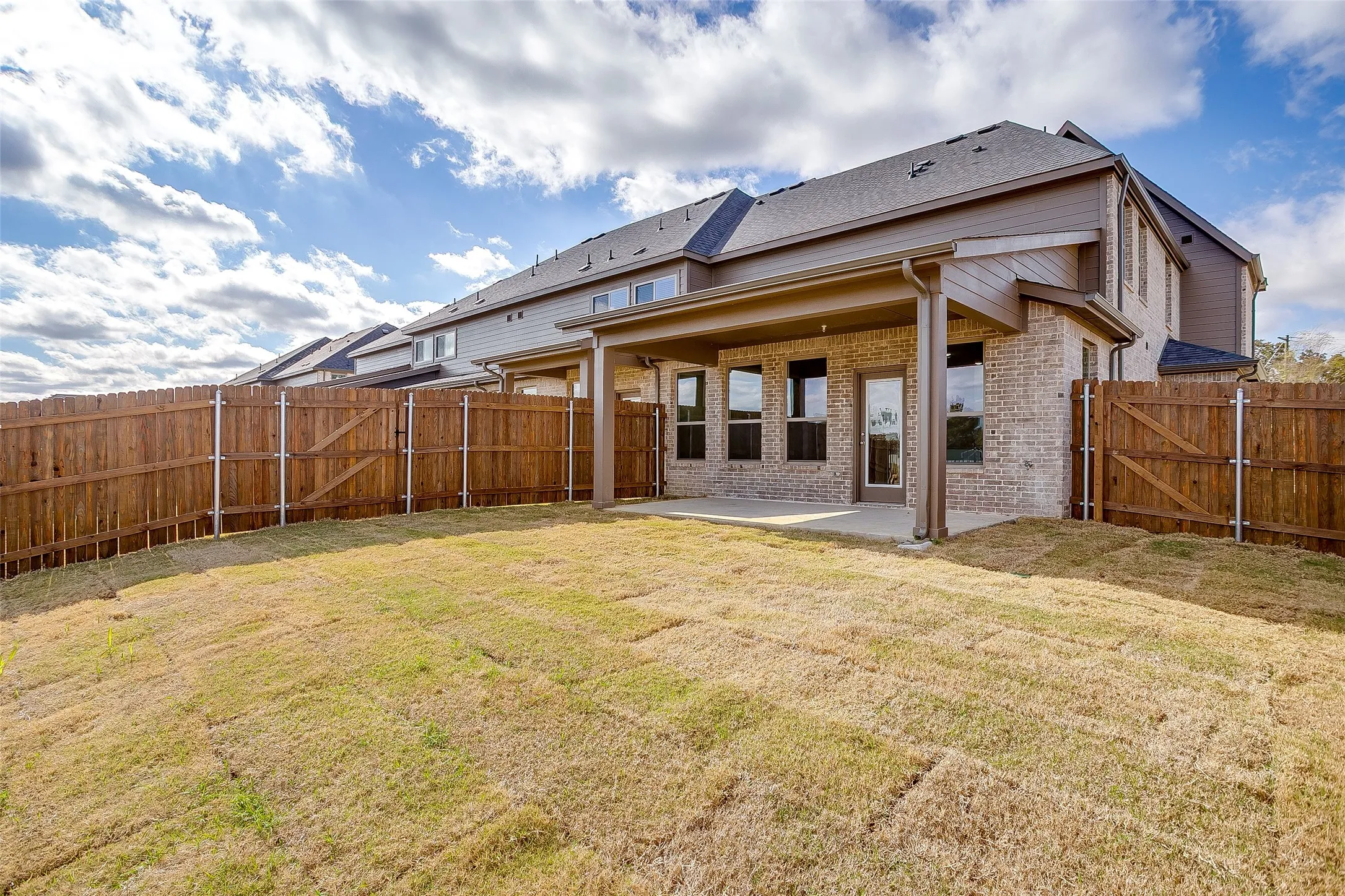 Back of house featuring a gate, brick siding, a patio, and a fenced backyard