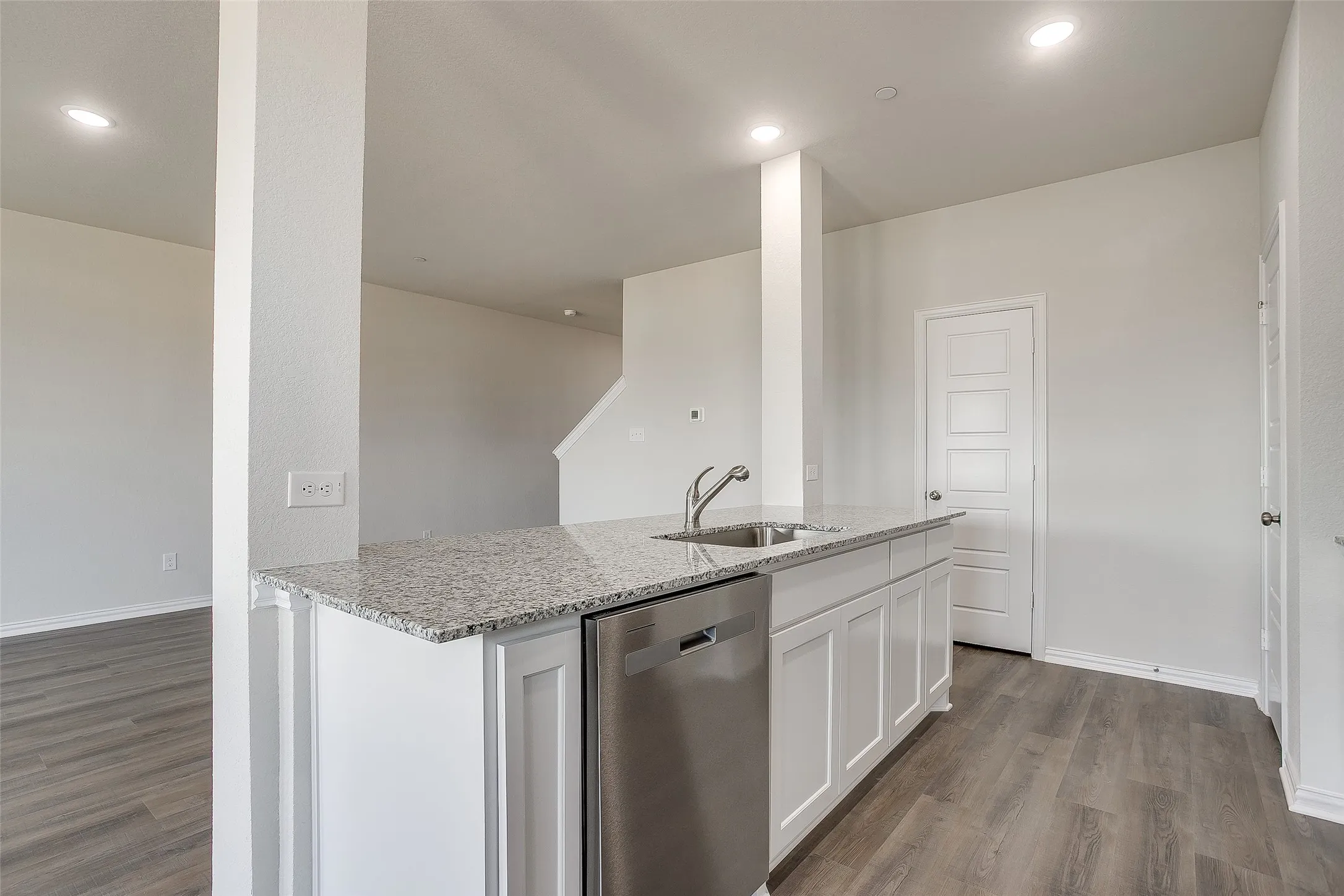 Kitchen featuring dark wood-style floors, white cabinets, dishwasher, light stone countertops, and a center island with sink