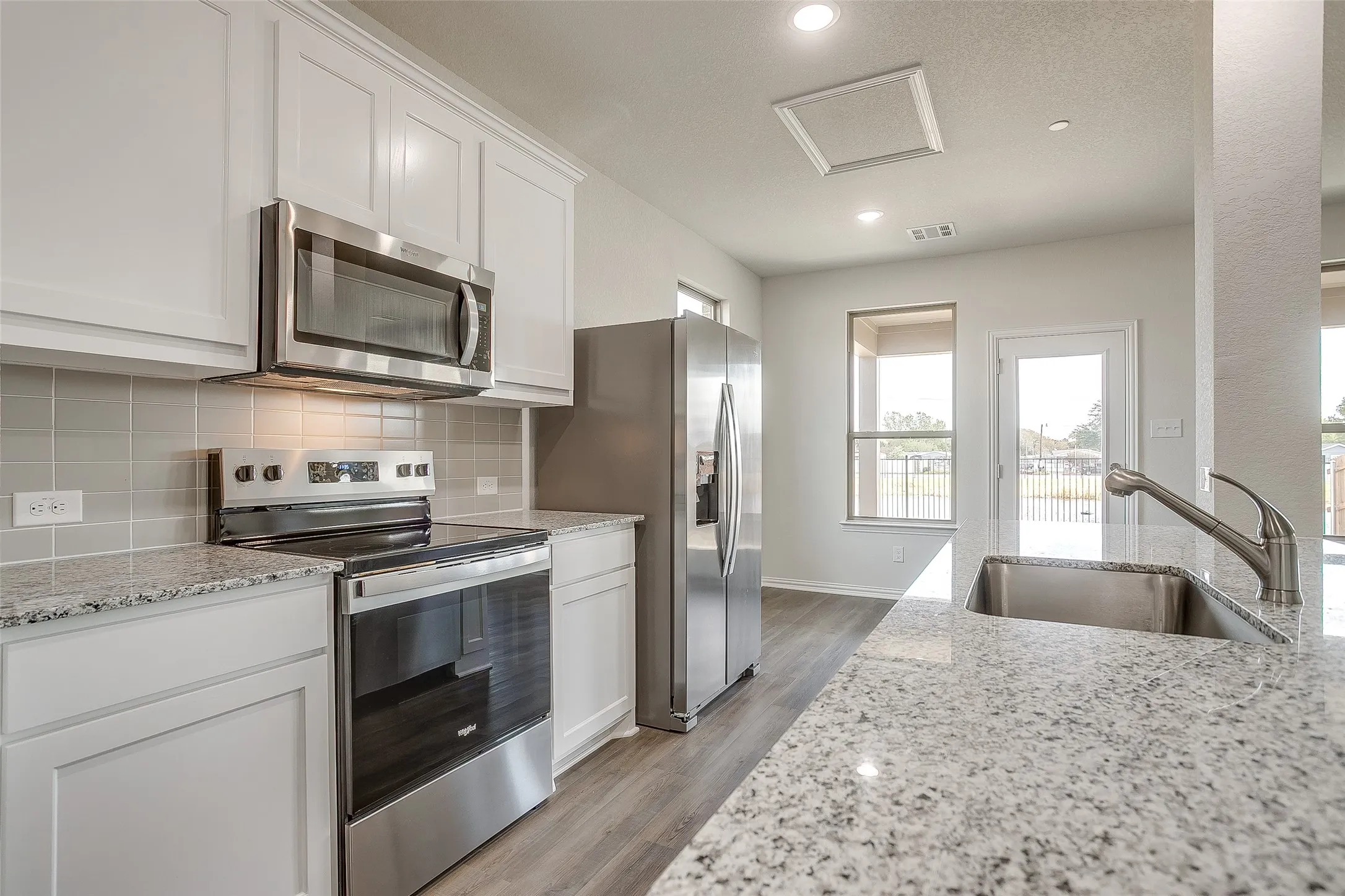 Kitchen with appliances with stainless steel finishes, light wood-style floors, light stone counters, white cabinetry, and recessed lighting