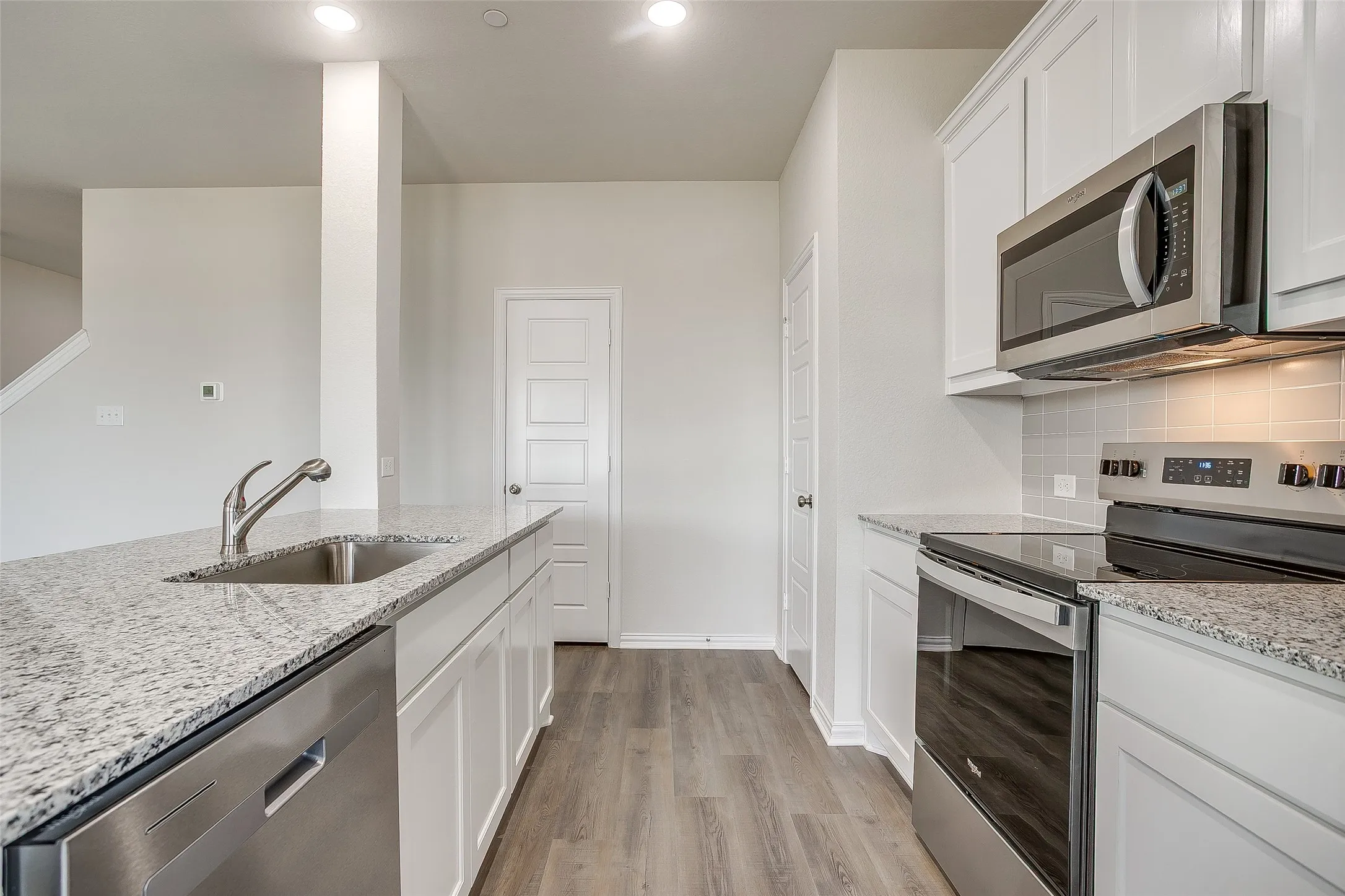 Kitchen with stainless steel appliances, white cabinets, light wood finished floors, light stone countertops, and recessed lighting