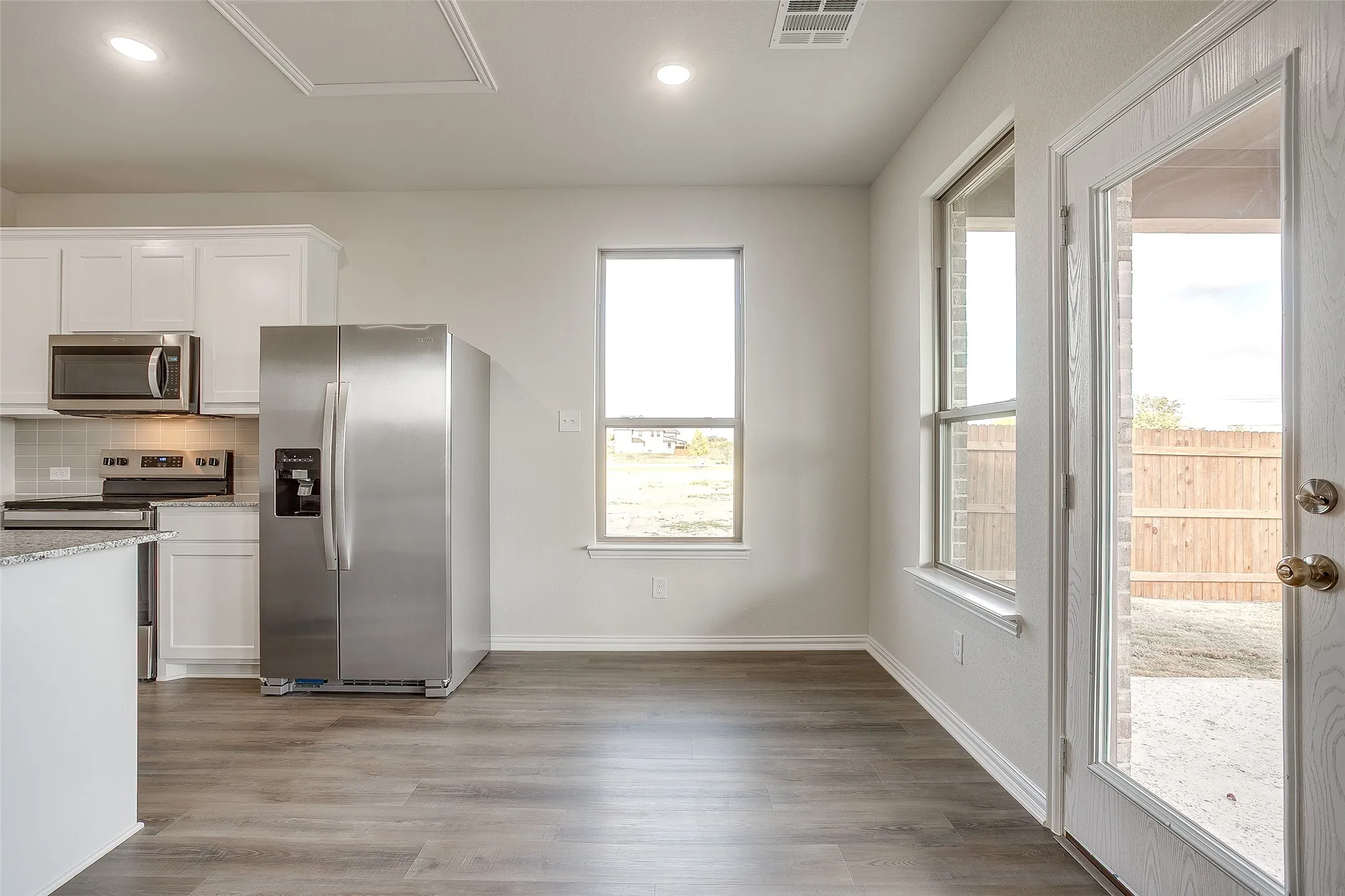 Kitchen featuring stainless steel appliances, decorative backsplash, white cabinets, dark wood-style flooring, and light stone counters