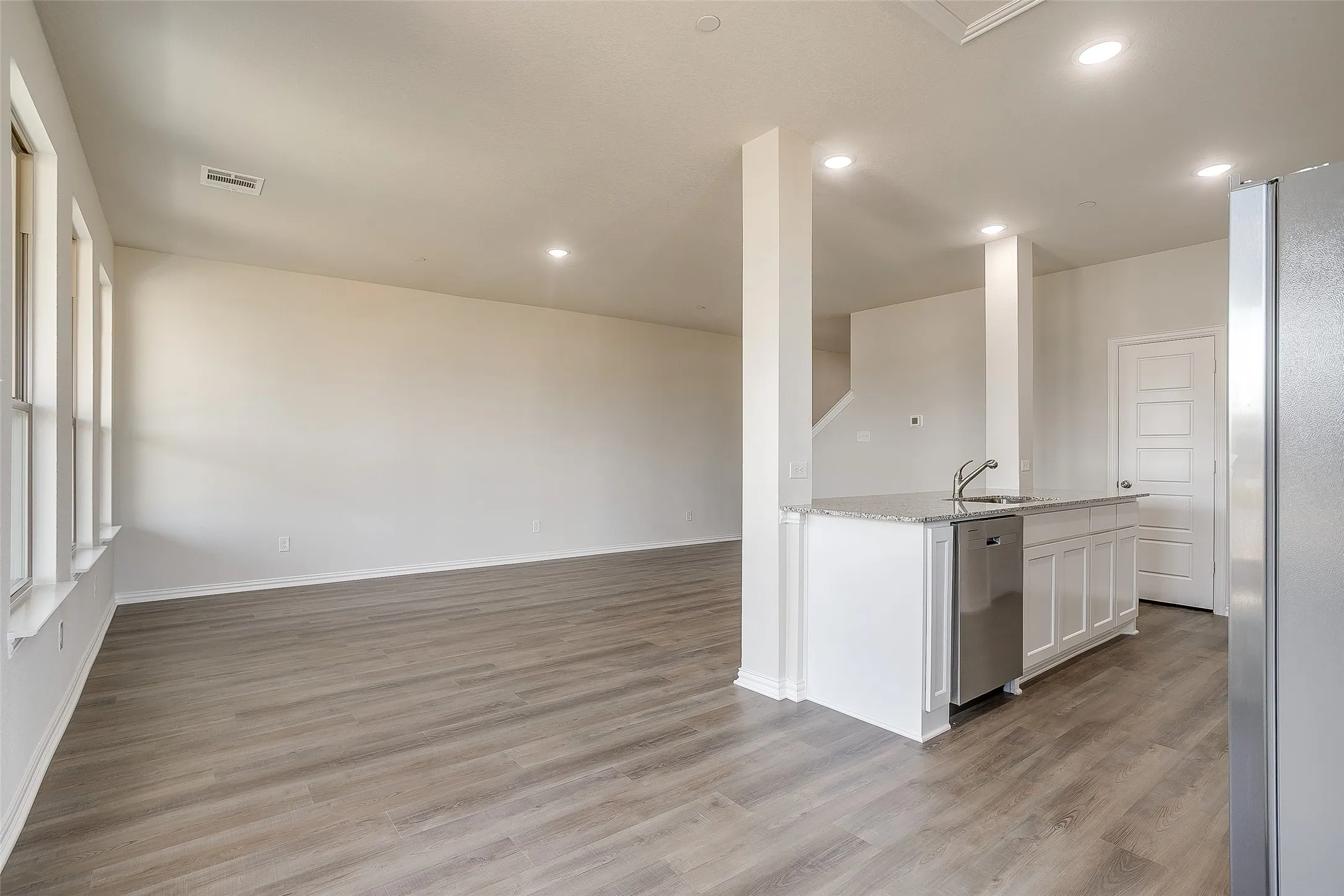 Kitchen featuring appliances with stainless steel finishes, light stone counters, light wood finished floors, a center island with sink, and white cabinetry