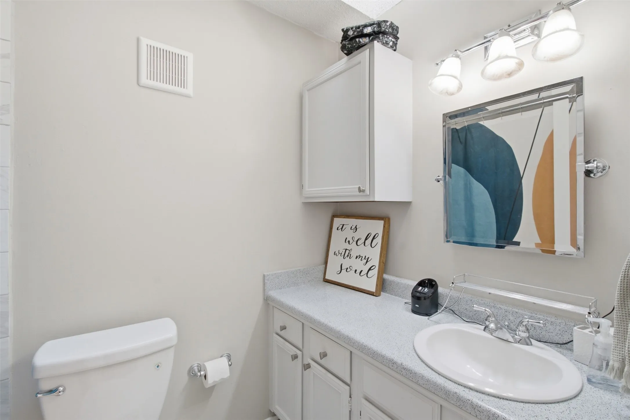 Bright bathroom featuring a curved oval sink with polished chrome faucet, white cabinetry with multiple drawers, quartz countertop, and dual vanity lighting