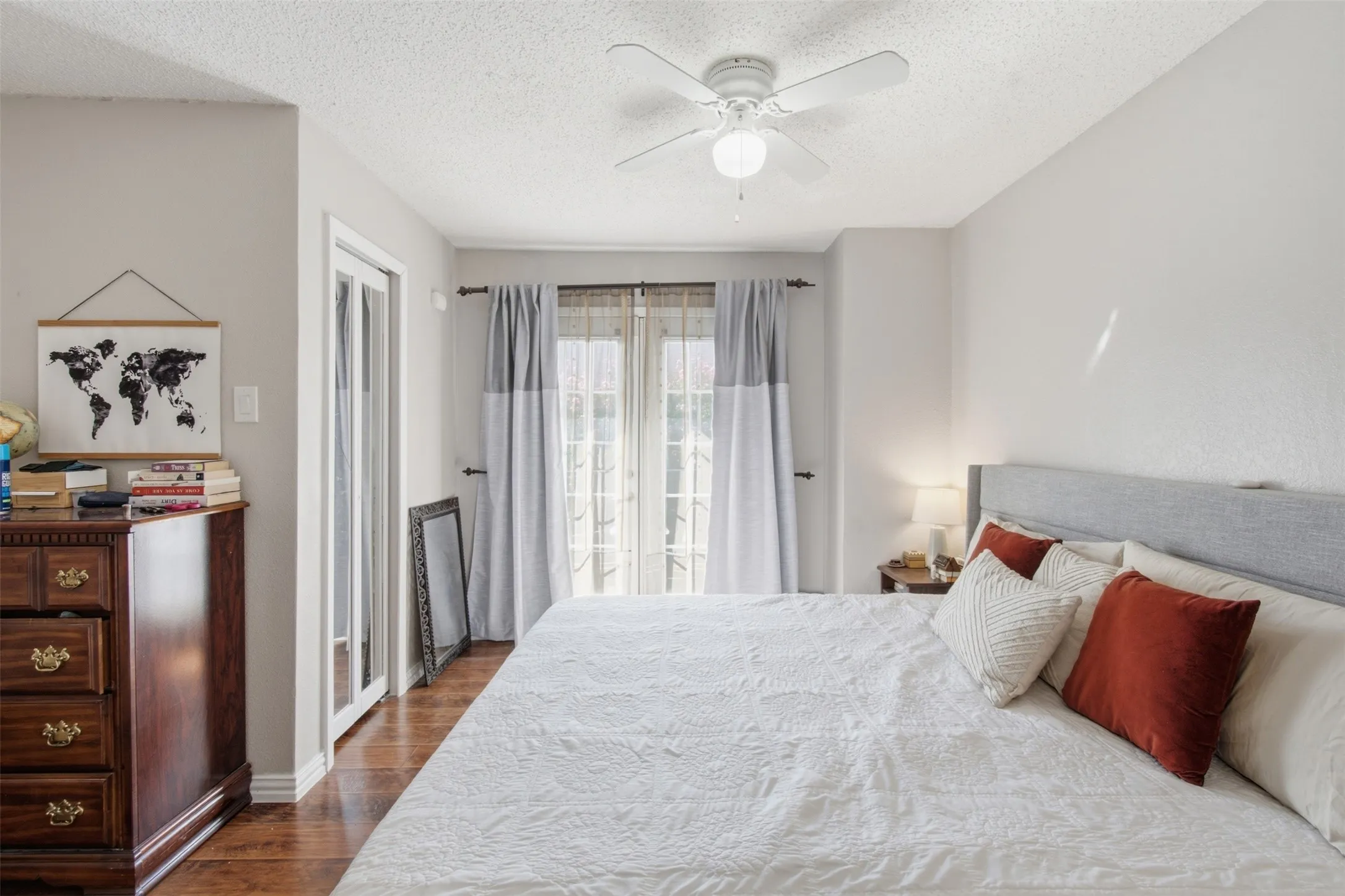 Bright primary bedroom featuring hardwood flooring, a gray upholstered headboard, and abundant natural light from glass doors and transom windows