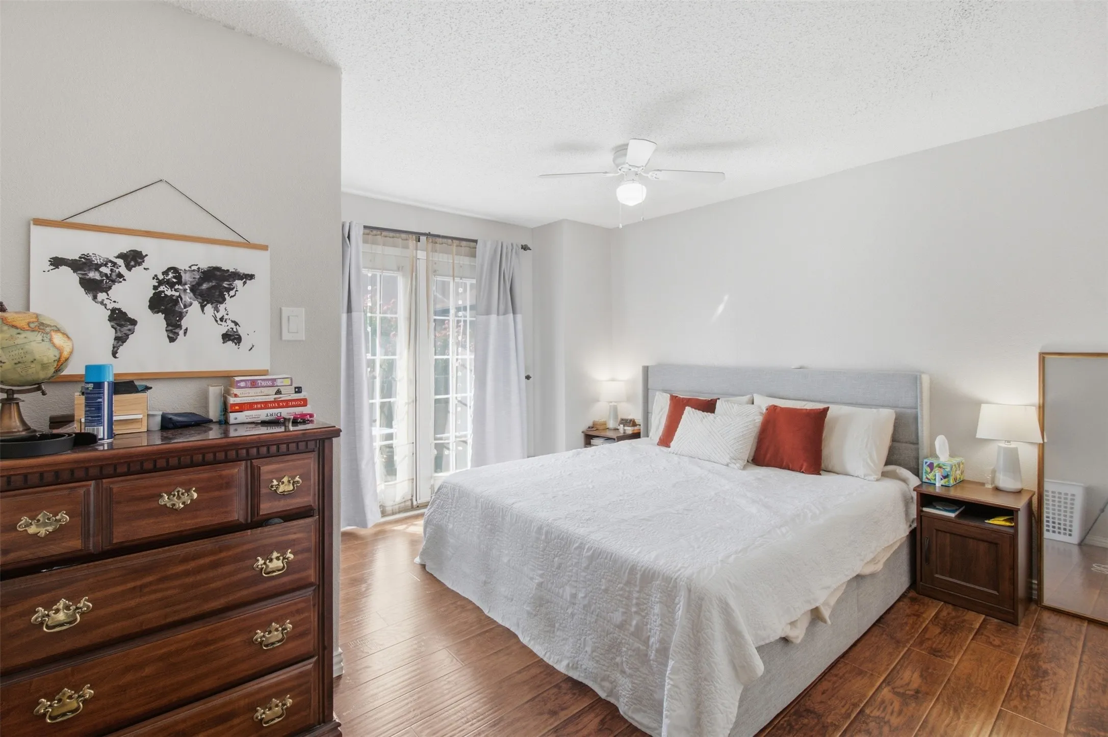 Spacious primary bedroom with hardwood flooring, ceiling fan with integrated lighting, and glass sliding doors providing natural light