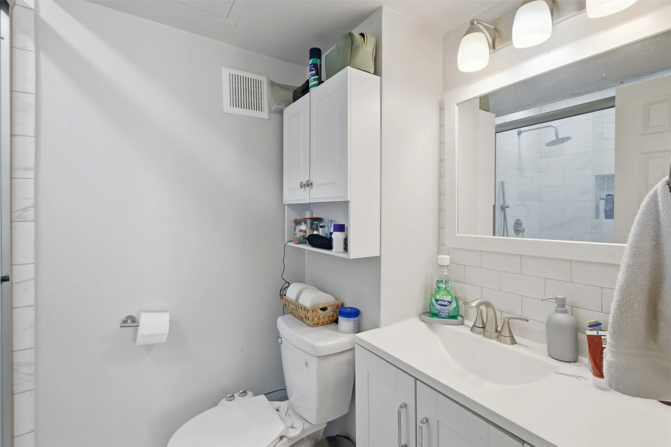 Clean and functional bathroom featuring a white vanity with ample counter space, recessed medicine cabinet with shelving, tile surround, and natural lighting from a large mirror-backed window
