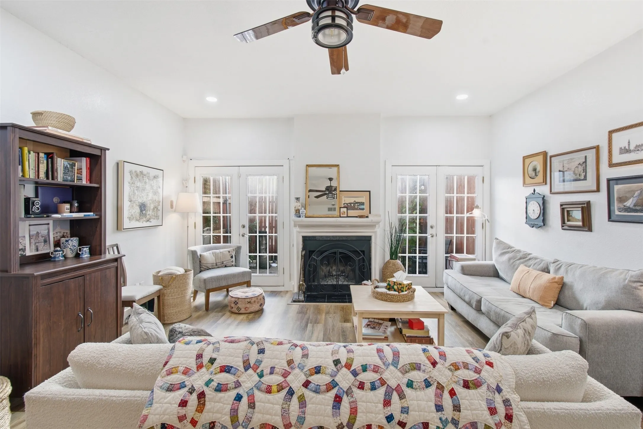 Bright and airy living room anchored by a wood-burning fireplace with black surround, offering multiple glass doors that flood the space with natural light
