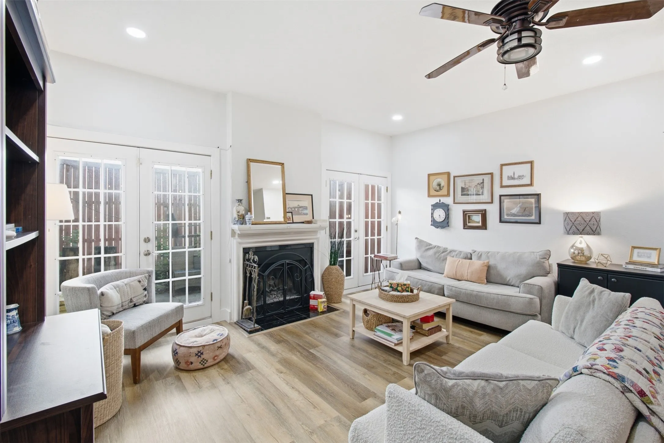 Bright, open living area featuring wood-finish flooring throughout, a gas fireplace with black surround, and abundant natural light from French doors and recessed ceiling fixtures