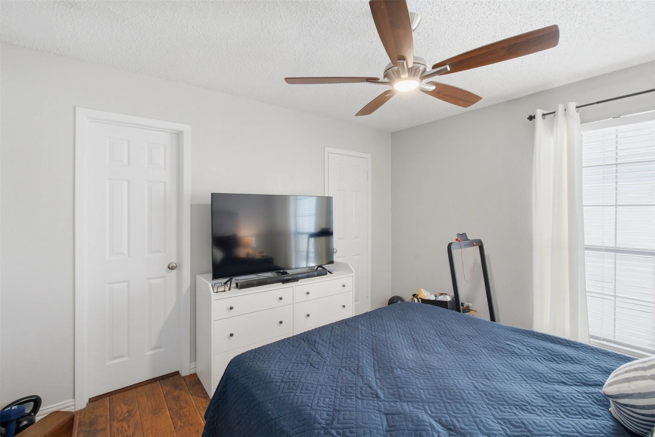 Spacious bedroom featuring hardwood flooring, a ceiling fan with integrated lighting, and ample natural light from large windows