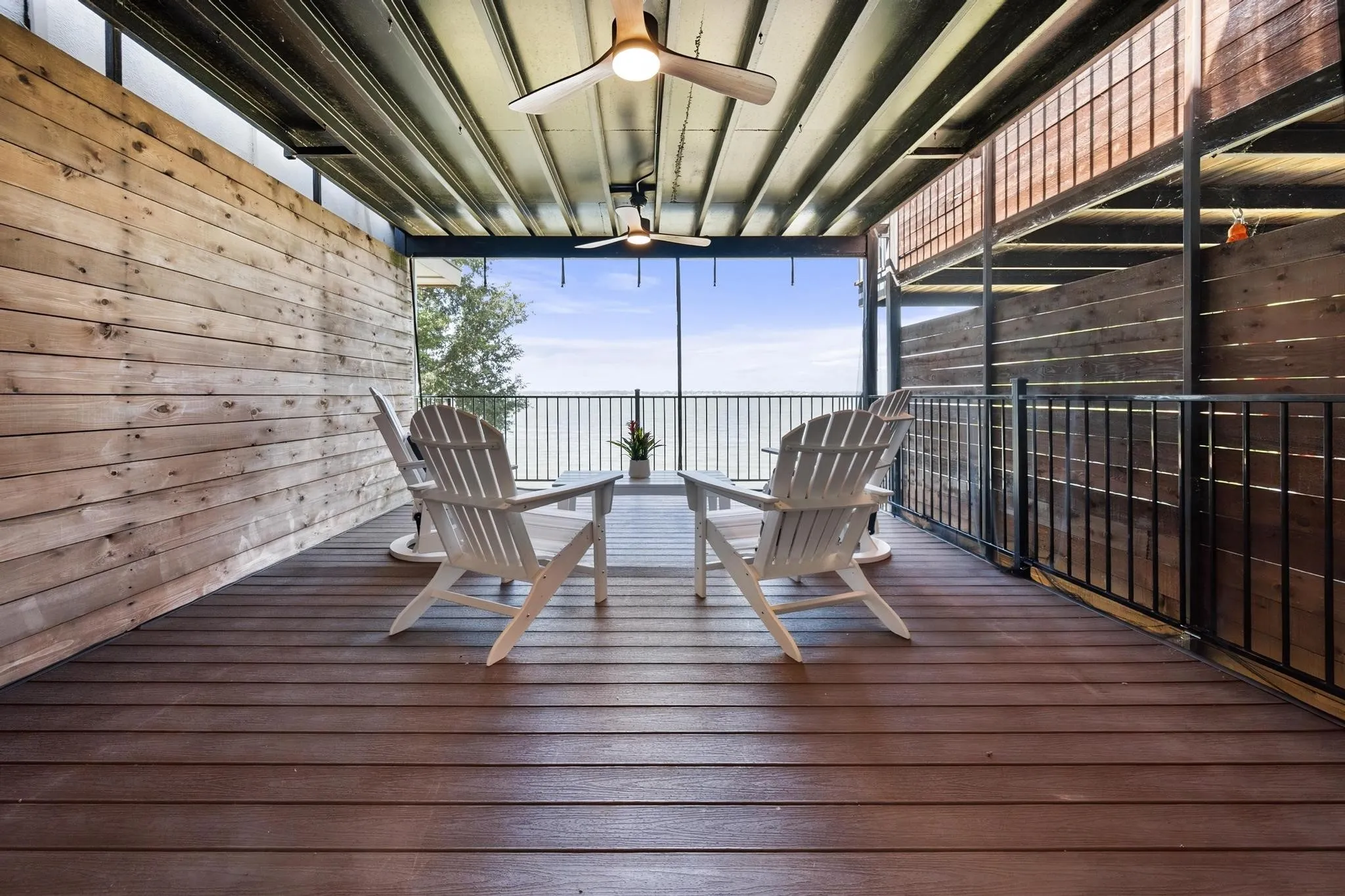 Covered patio with a wood-finish deck, horizontal plank siding, and integrated ceiling fans
