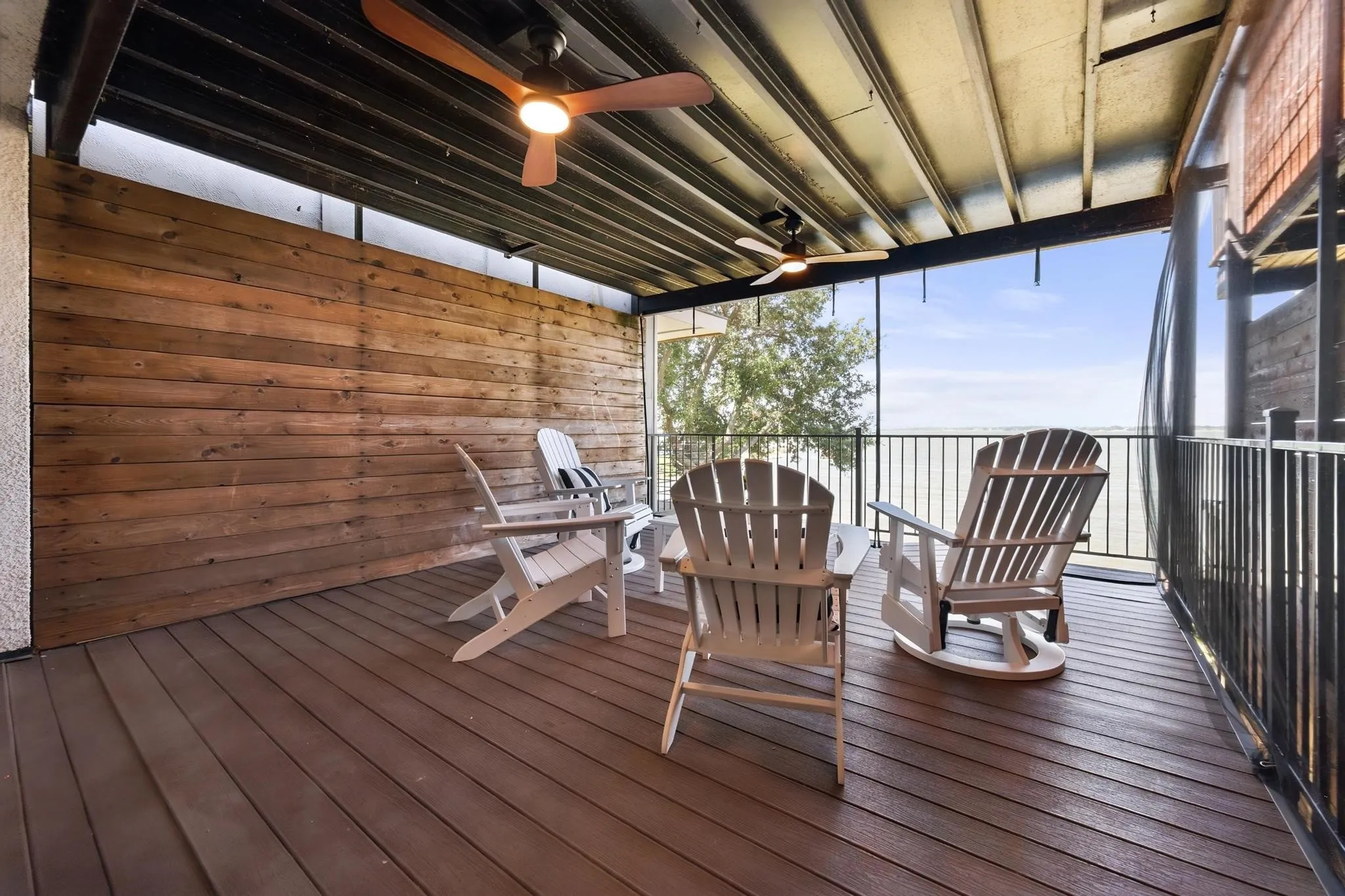 Covered outdoor deck with wood-finish flooring, wood plank accent wall, and ceiling fans