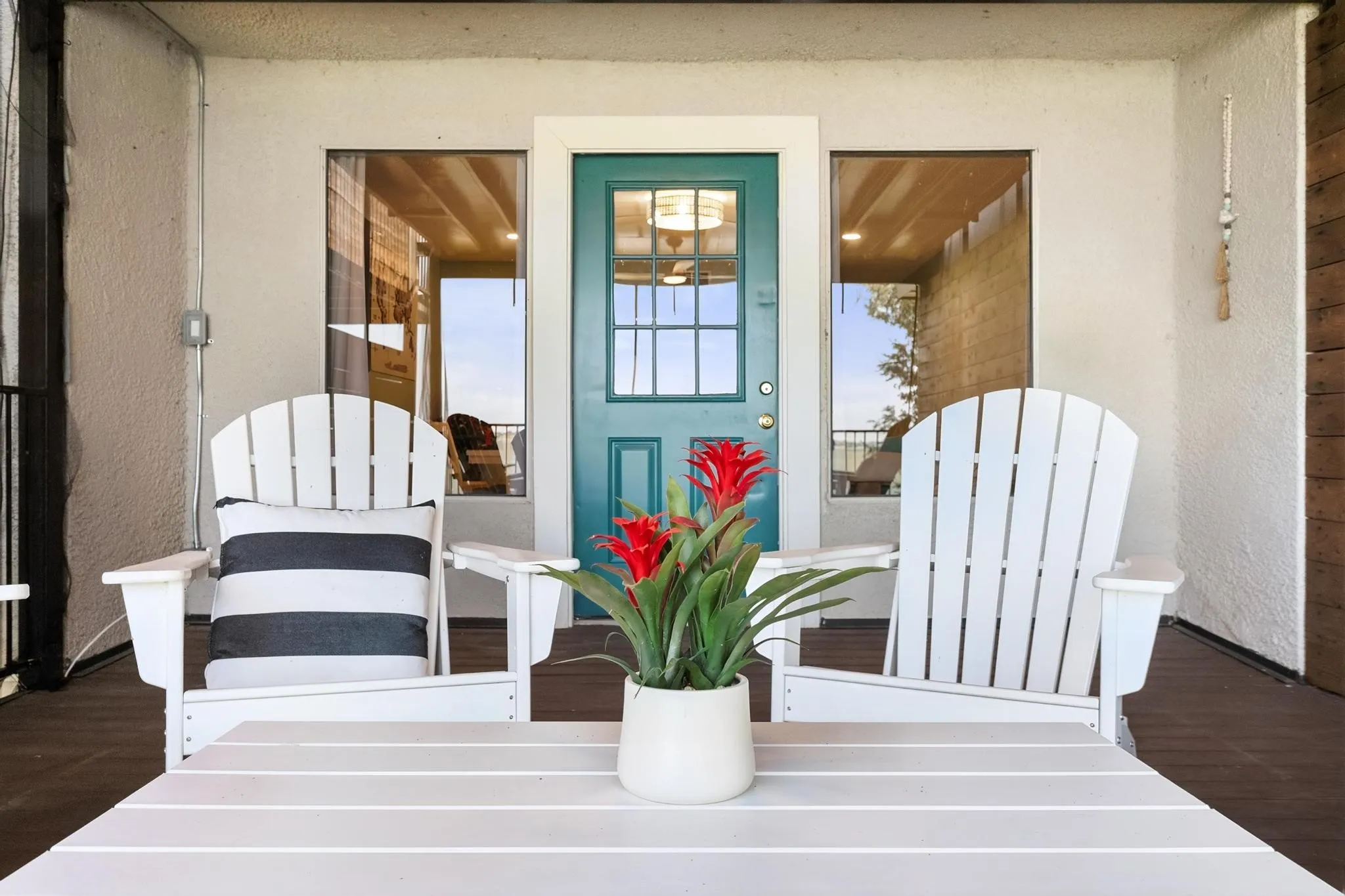 Covered front porch featuring a teal paneled door, two adjacent windows, and wood-finish flooring