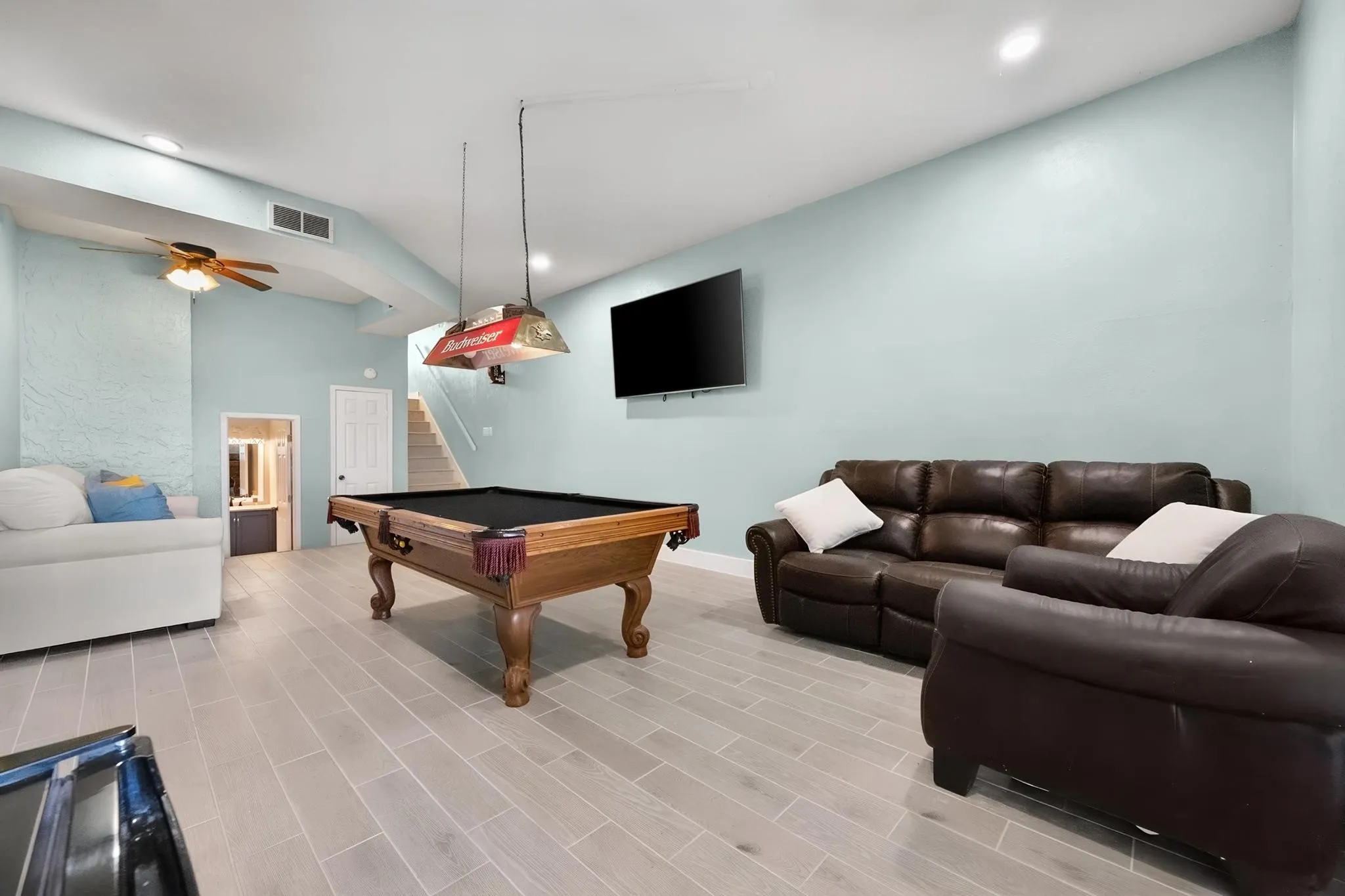 Spacious room featuring light wood-finish flooring, a ceiling fan, and a mounted flat-screen television
