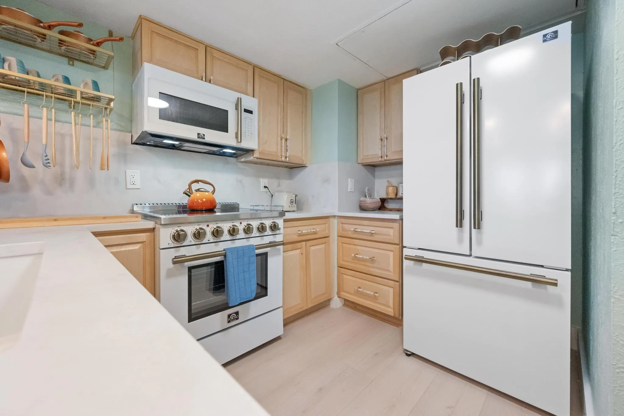 Hardwood cabinetry, stone countertops, stainless steel range with overhead microwave, and a French door refrigerator