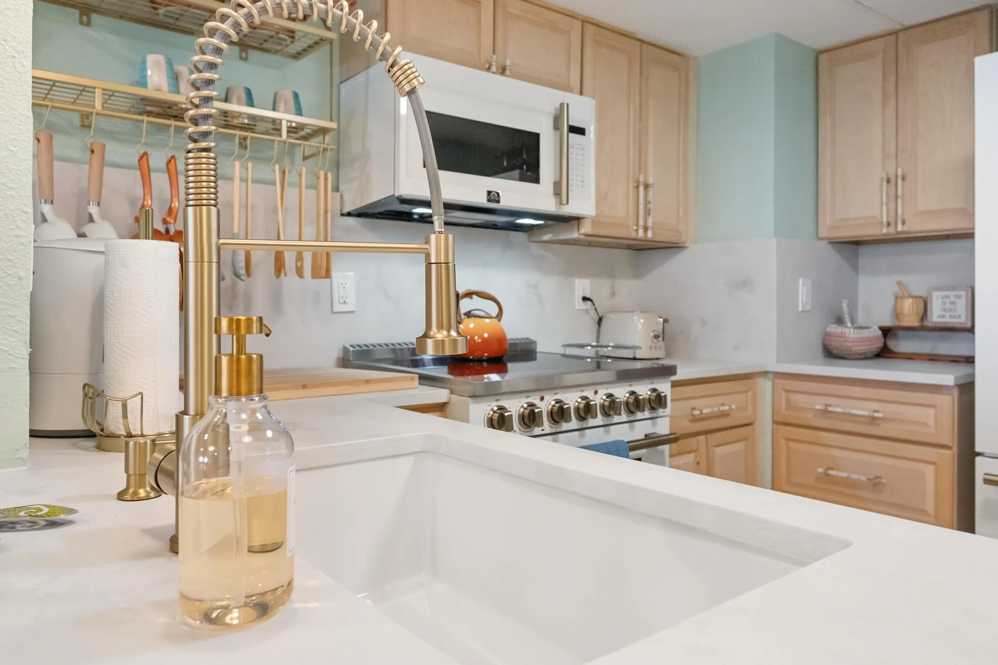 Kitchen featuring light wood cabinetry, a built-in microwave, a stainless steel range with a ventilation hood, and solid surface countertops