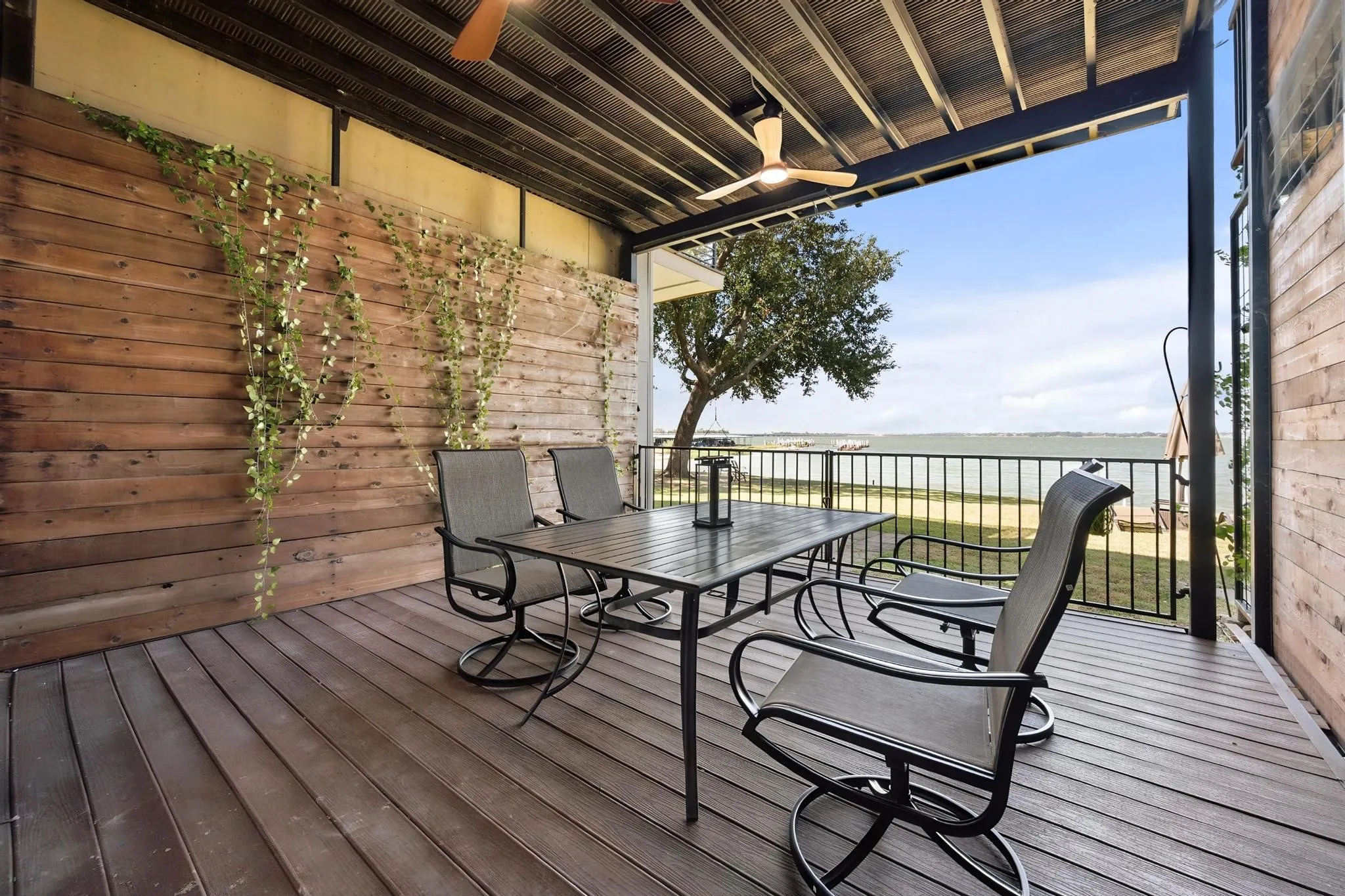 Covered outdoor deck with wood-finish flooring, a wood-paneled accent wall, and a ceiling fan