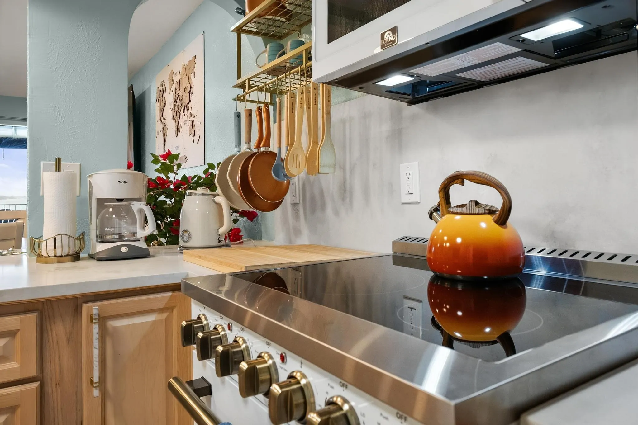 Cooktop with integrated range hood, light wood-finish cabinetry, light-toned countertops, and wall-mounted shelving