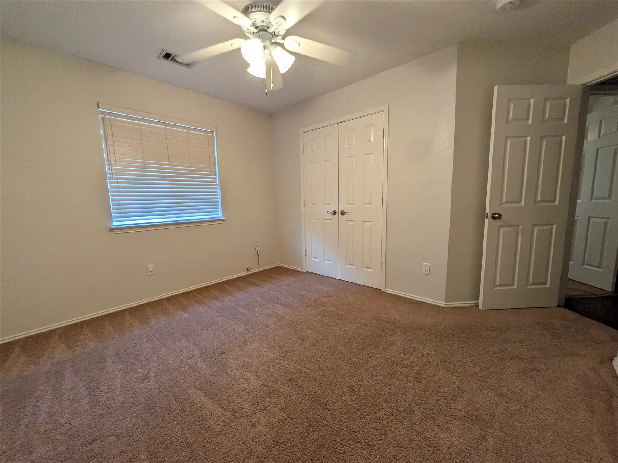 Plush carpeting, a ceiling fan with integrated lighting, and a window with blinds