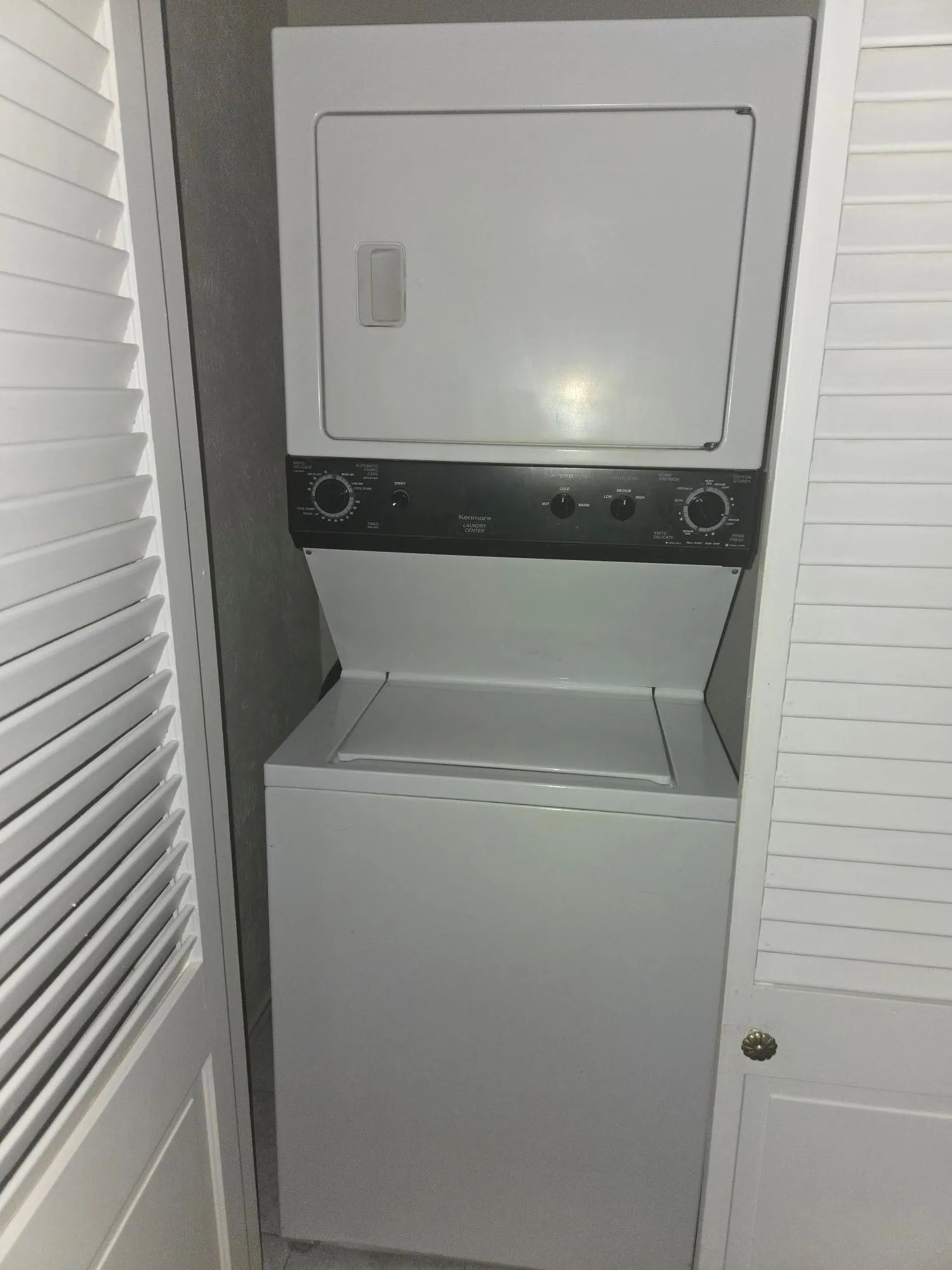 White stacked washer and dryer unit with louvered bi-fold doors