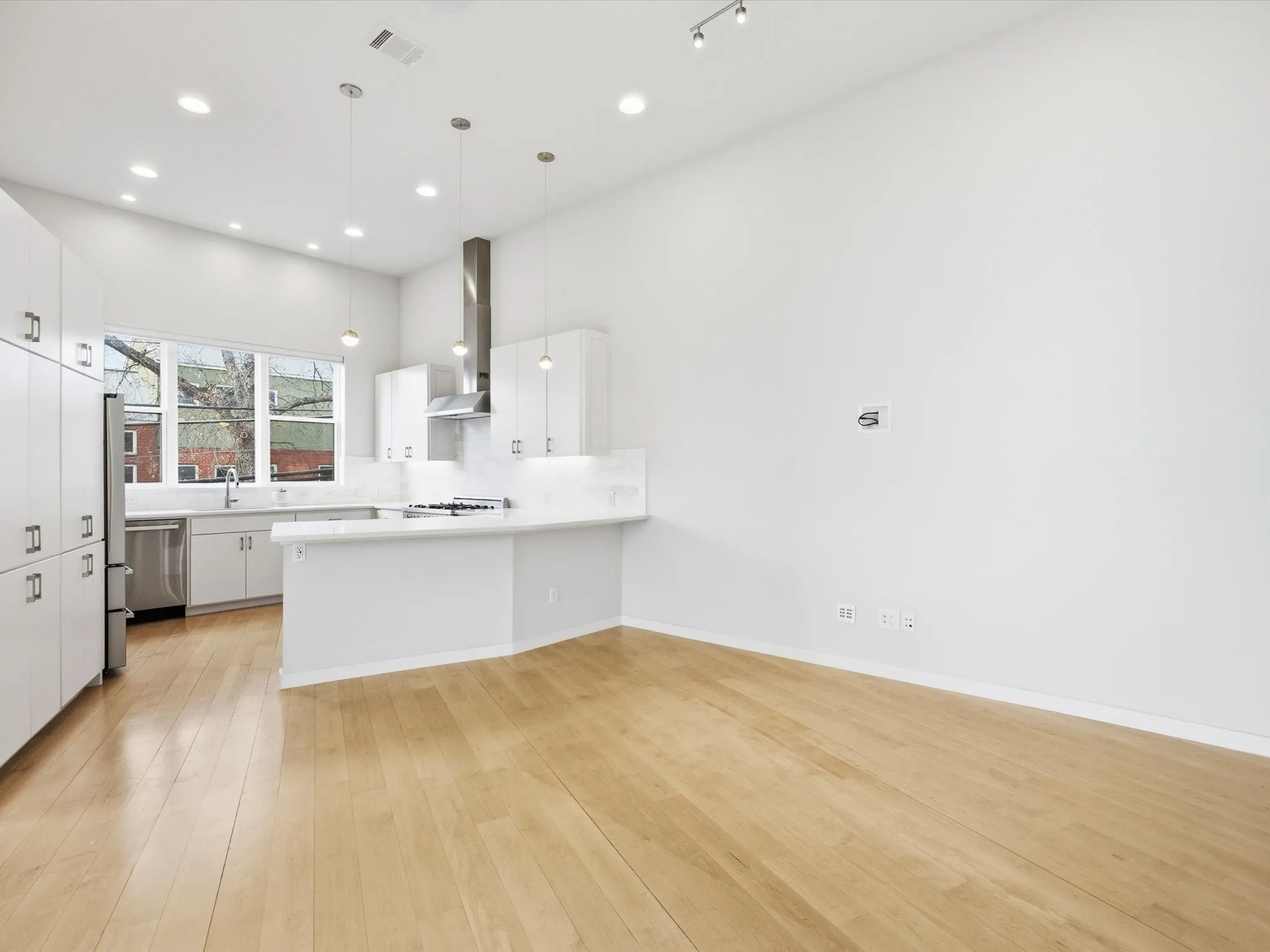 Kitchen with a peninsula, white cabinetry, pendant lighting, light wood finished floors, and appliances with stainless steel finishes
