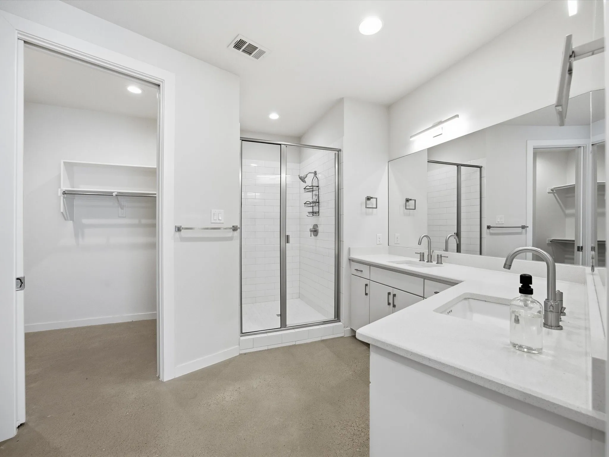 Bathroom with a spacious closet, double vanity, recessed lighting, finished concrete floors, and a stall shower