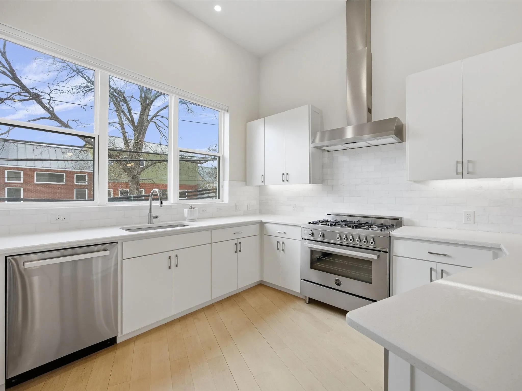Kitchen featuring stainless steel appliances, white cabinets, wall chimney range hood, light wood-type flooring, and light stone countertops