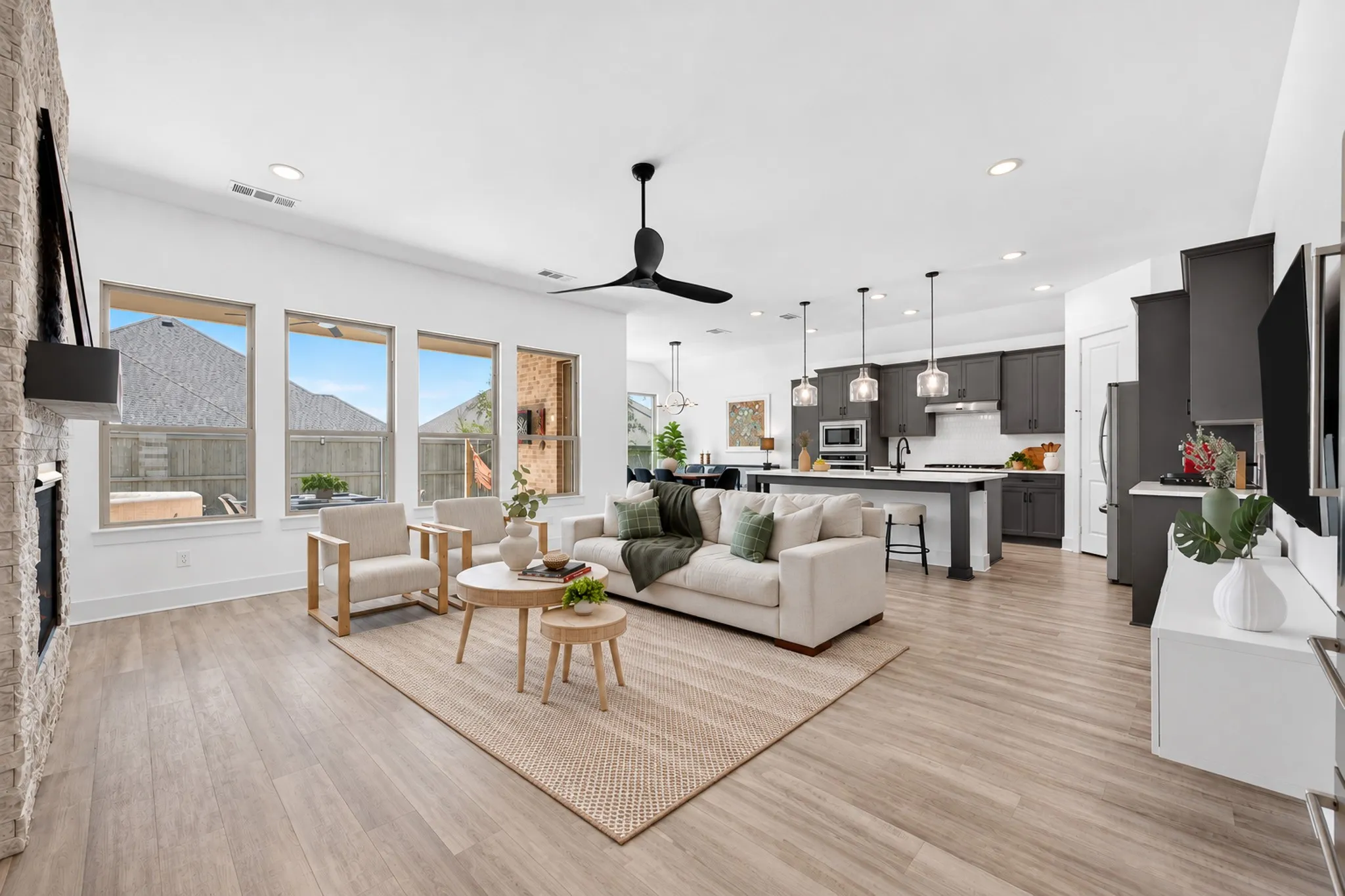 Open-concept living area with wood-finish flooring, a stone-clad fireplace, and multiple windows