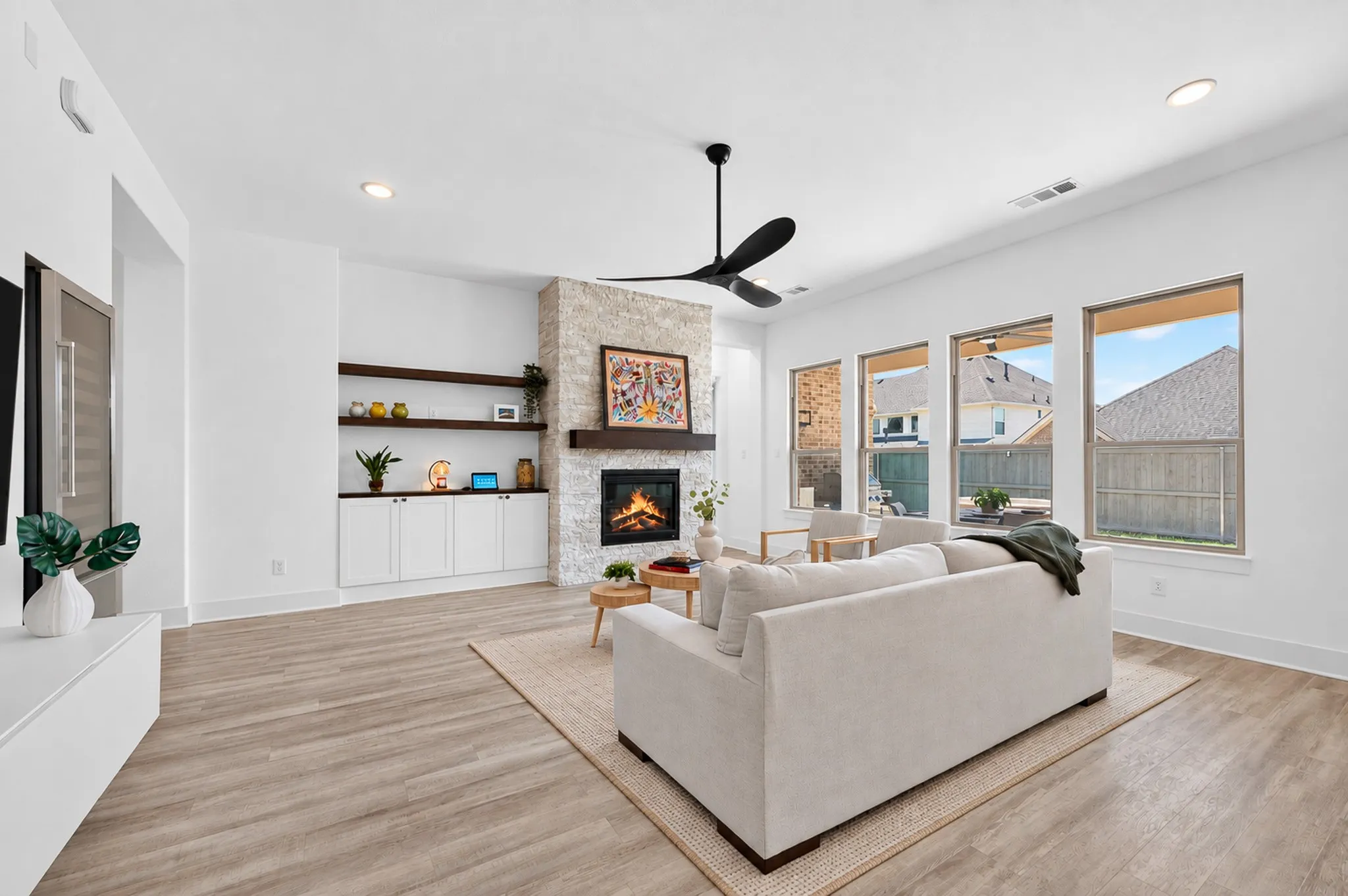 Spacious living area featuring a stone-clad fireplace with a wood mantel, built-in shelving, white cabinetry, and wood-finish flooring