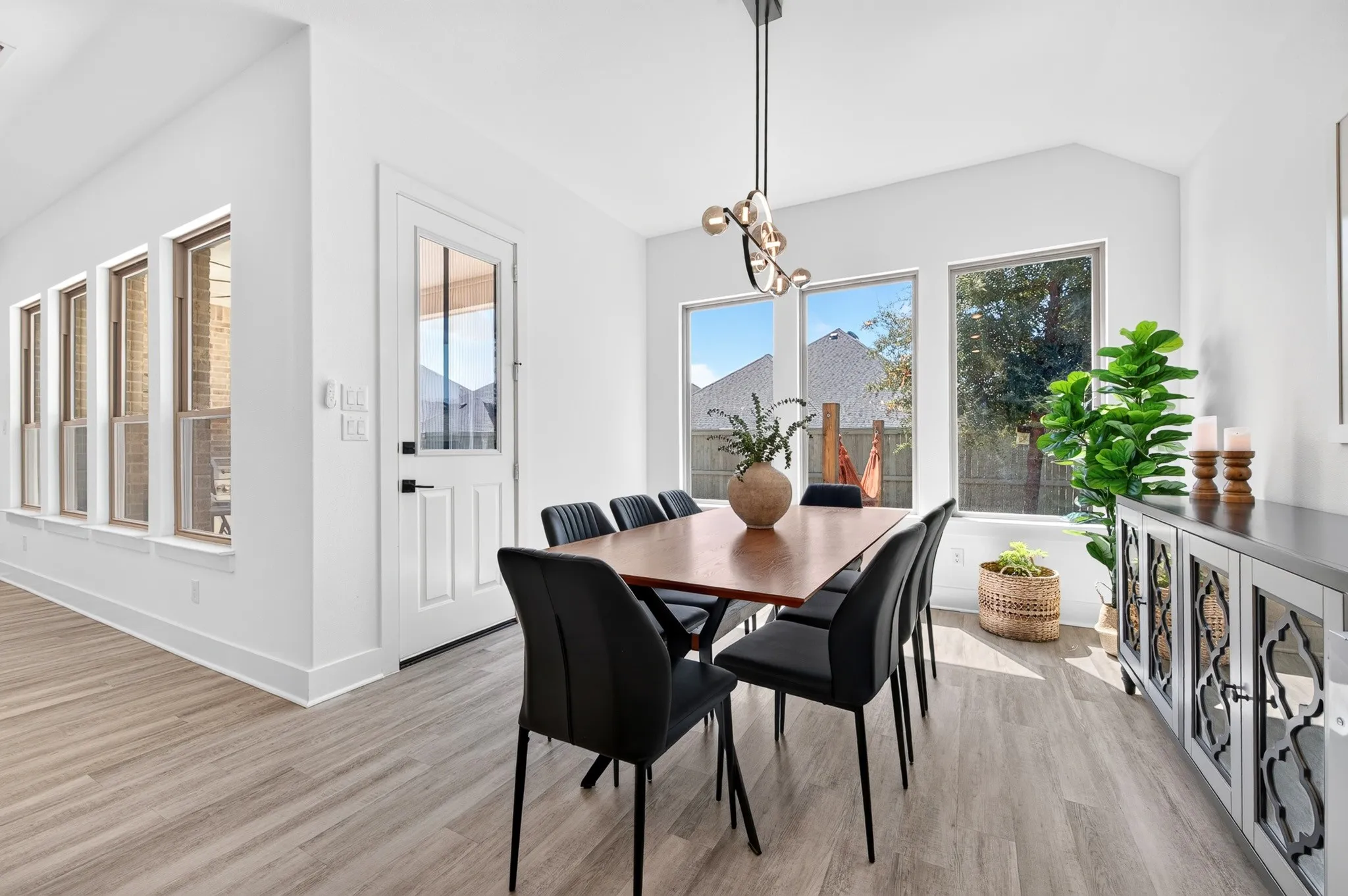 Wood-finish flooring throughout, multiple windows, contemporary pendant lighting, and a built-in sideboard with decorative doors